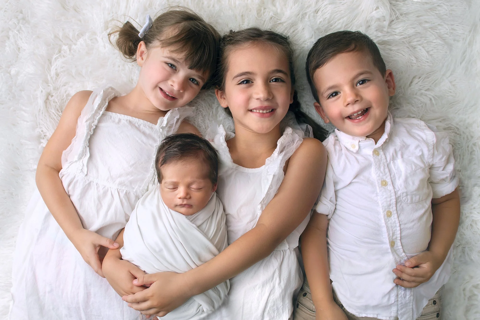 Ponte Vedra FL baby photographer with brothers and sisters in white clothes on white flokati background with baby boy