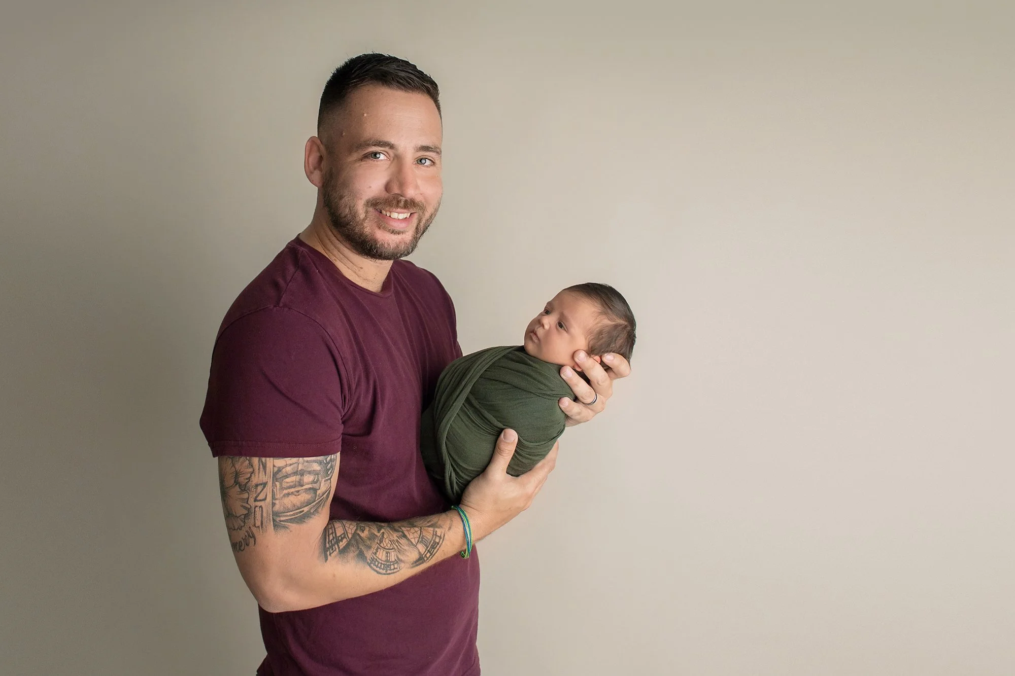 Ponte Vedra baby photographer in luxury studio with dad holding newborn boy on neutral background with tattoo arms