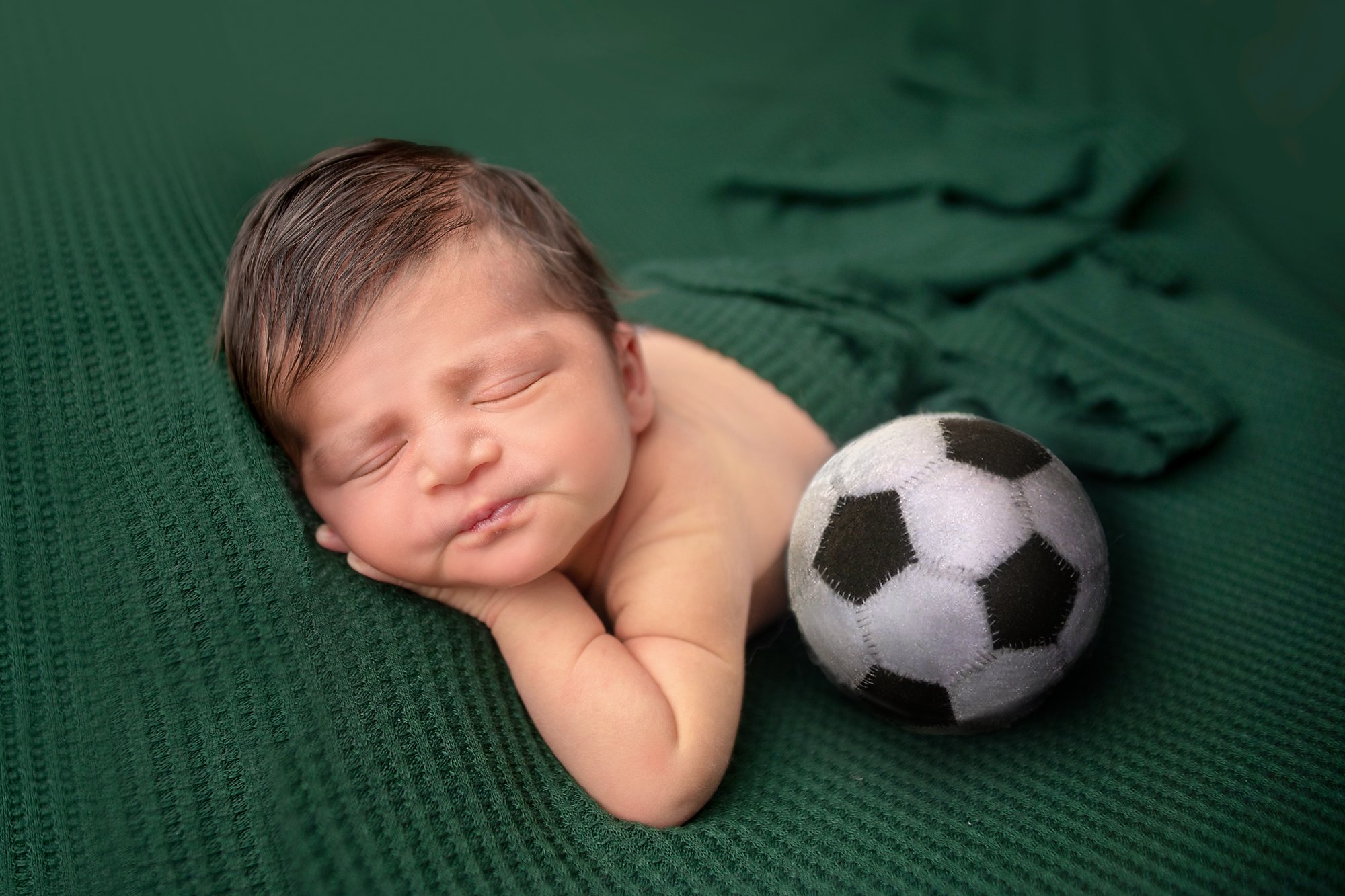 Baby newborn boy with soccer ball on green backdrop with wrap and lots of hair in Ponte Vedra photo studio