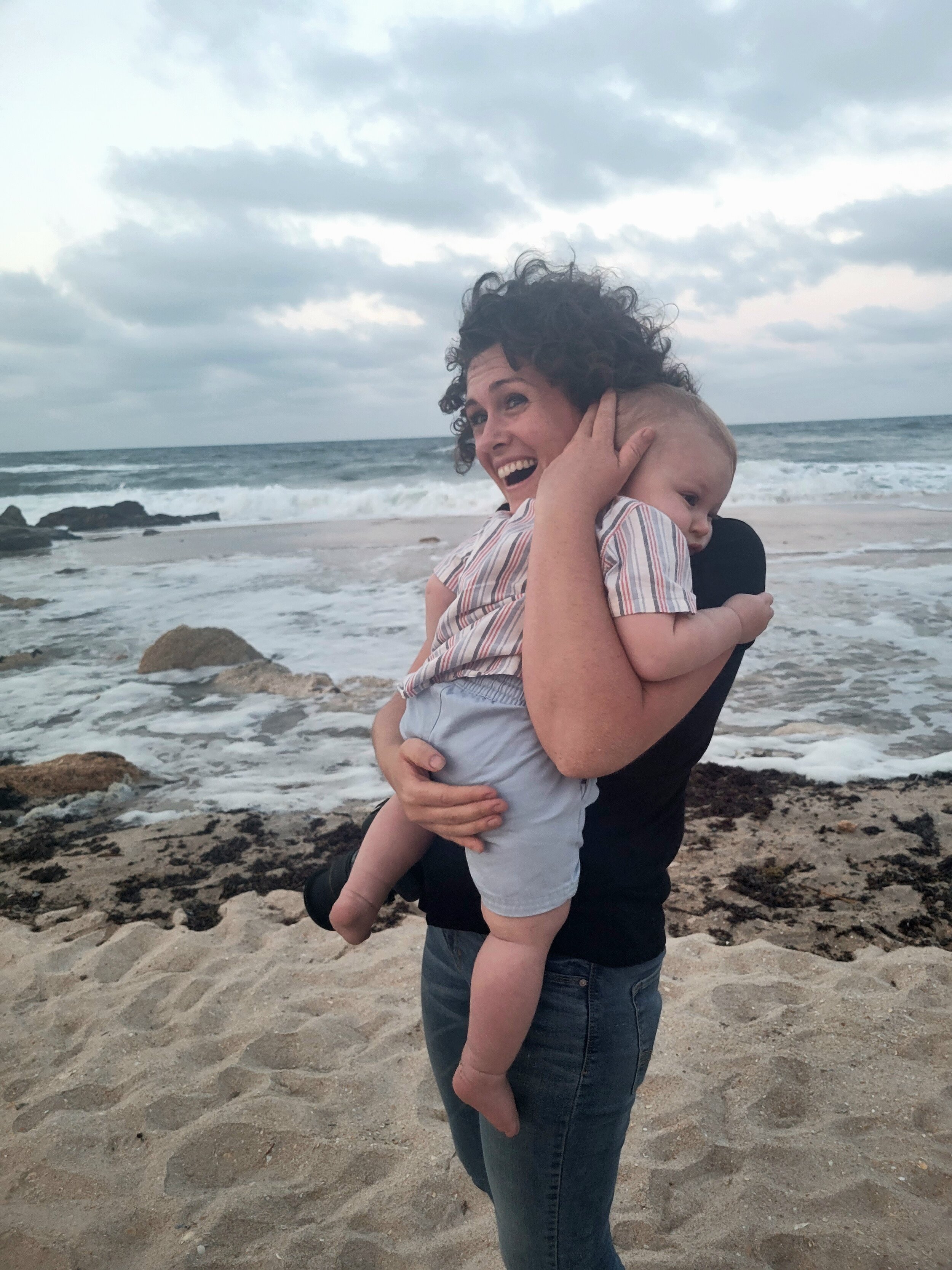 Best vacation beach photographer in St. Augustine FL holding a baby on a sandy beach with ocean waves in the background.