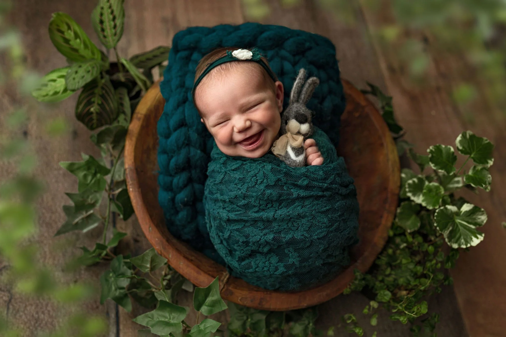 Smiling baby in wooden bowl with ivy, greenery, natural wood during a newborn photo shoot in St. Augustine, FL