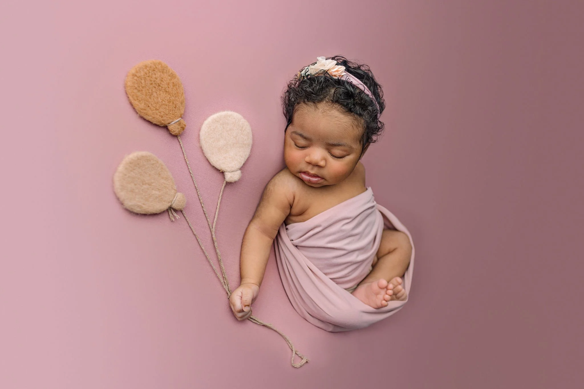 African American baby girl on pink background with felt prop balloons during newborn photos in portrait studio located in St. Aug, FL 32080