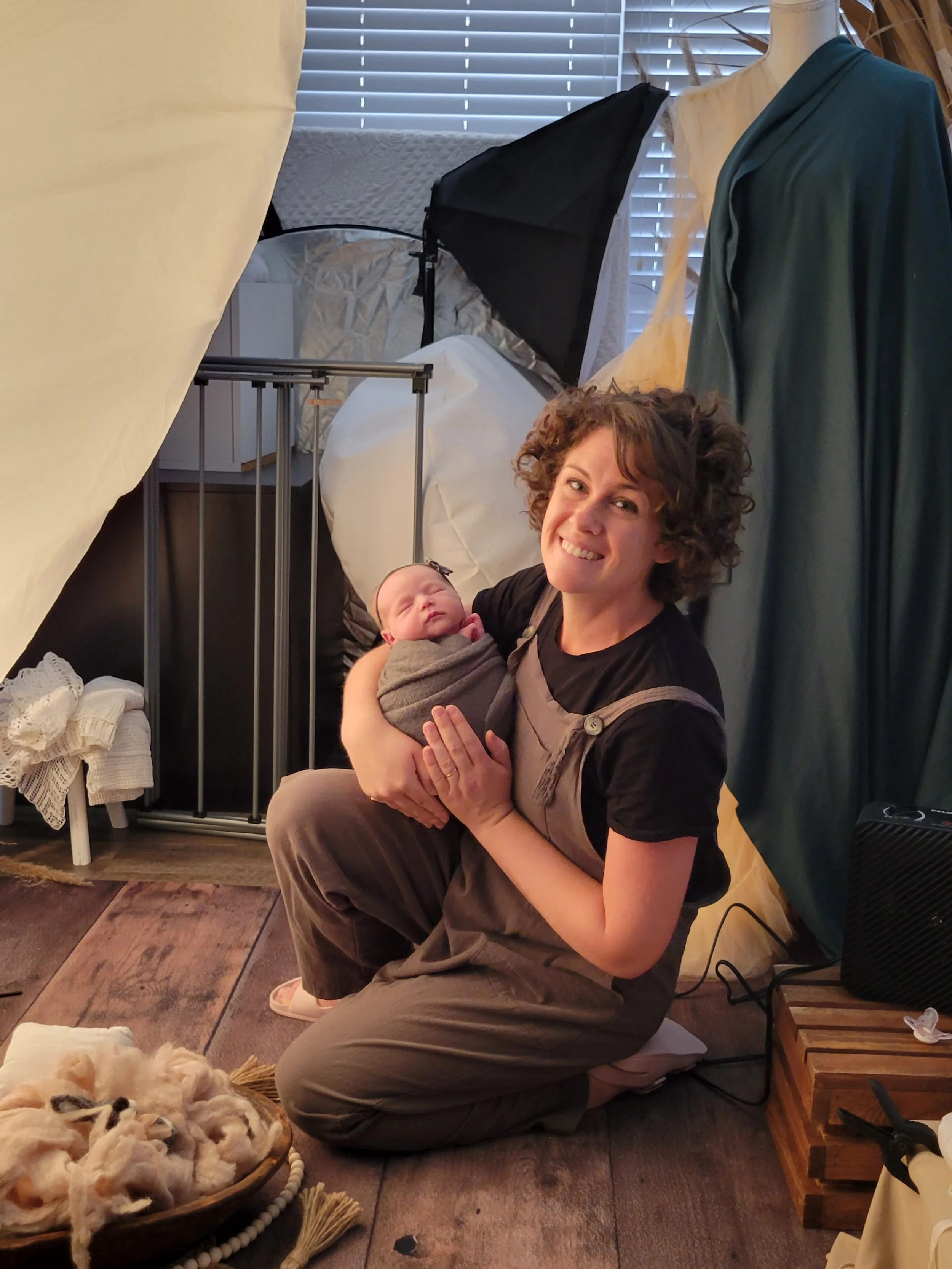 Jacksonville, FL portrait photographer holding a swaddled newborn in a photography studio setup, with lighting equipment and props visible in the background.