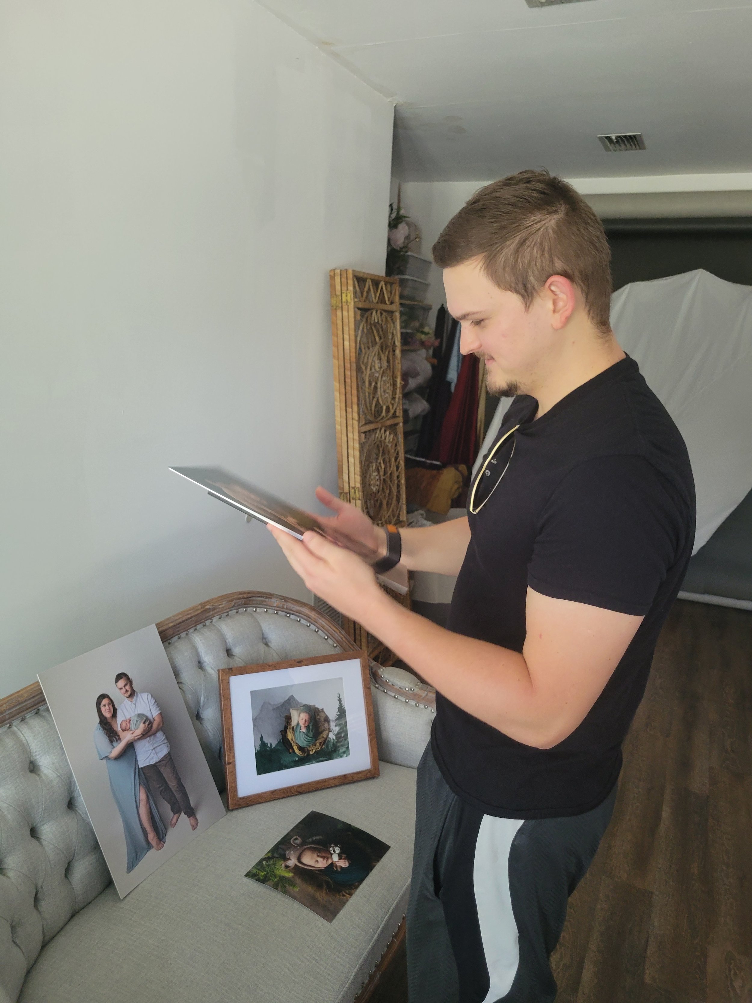 Father standing in newborn photo studio in Jacksonville, FL looking at baby pictures with framed family photo and luxury photo album
