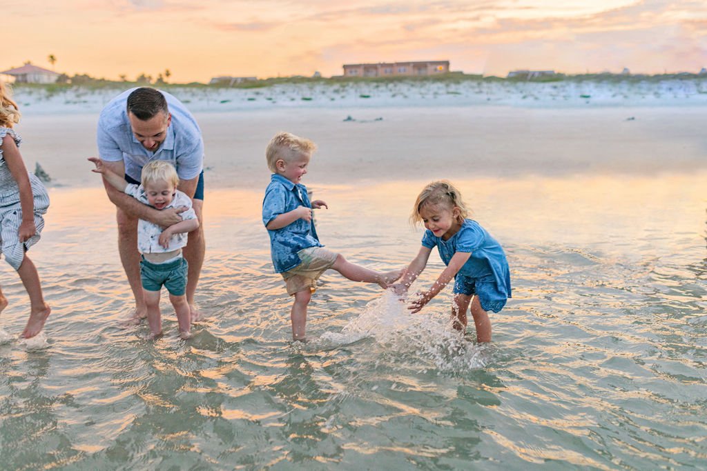 Sunset beach photo shoot in St. Augustine FL with family with kids wearing blue and khaki and playing with toddler in water
