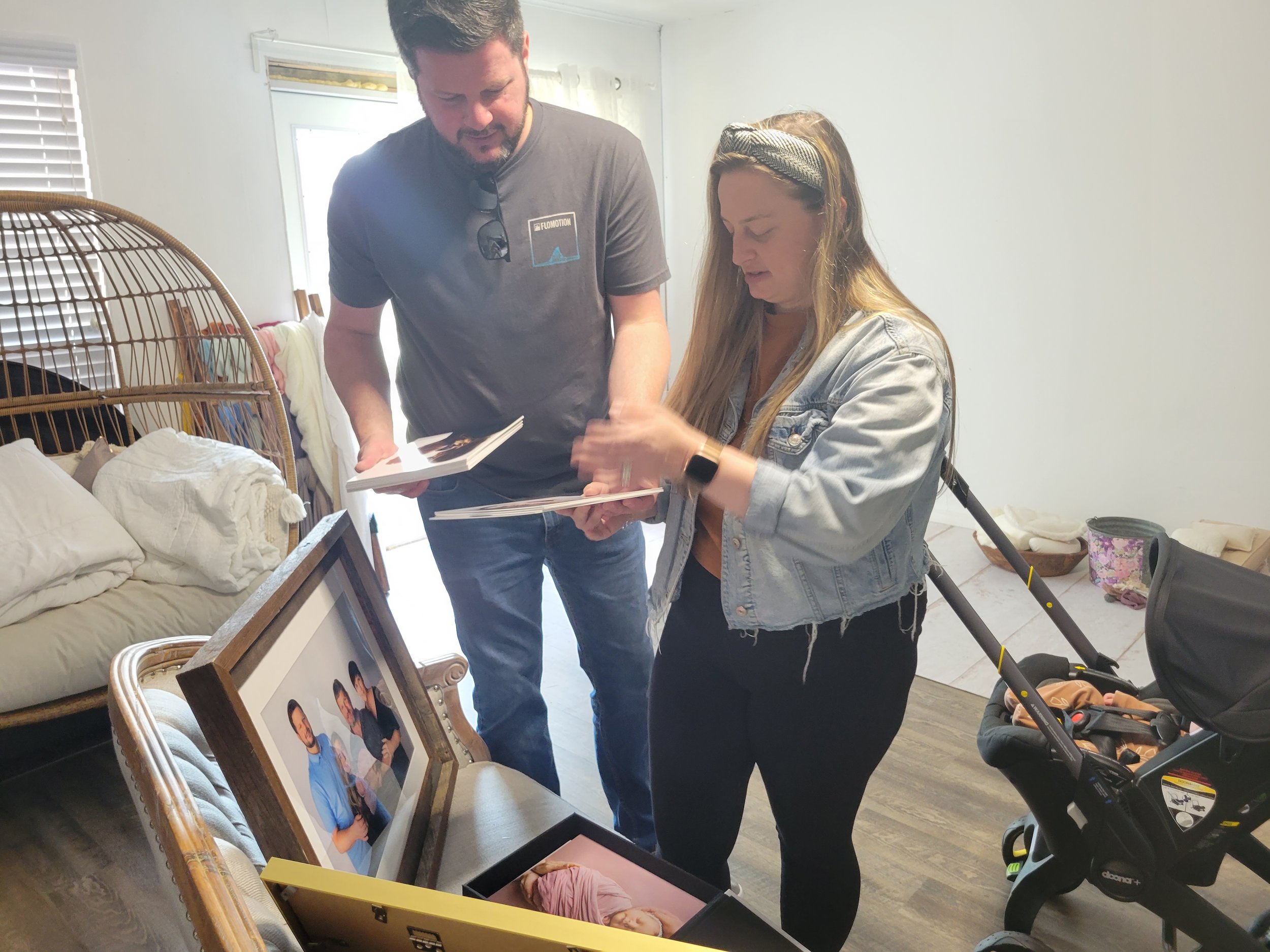 Family looking at IVF newborn photos in St. Augustine, FL photography studio. Framed photos with picture of mom and dad with baby on white background and quality props.