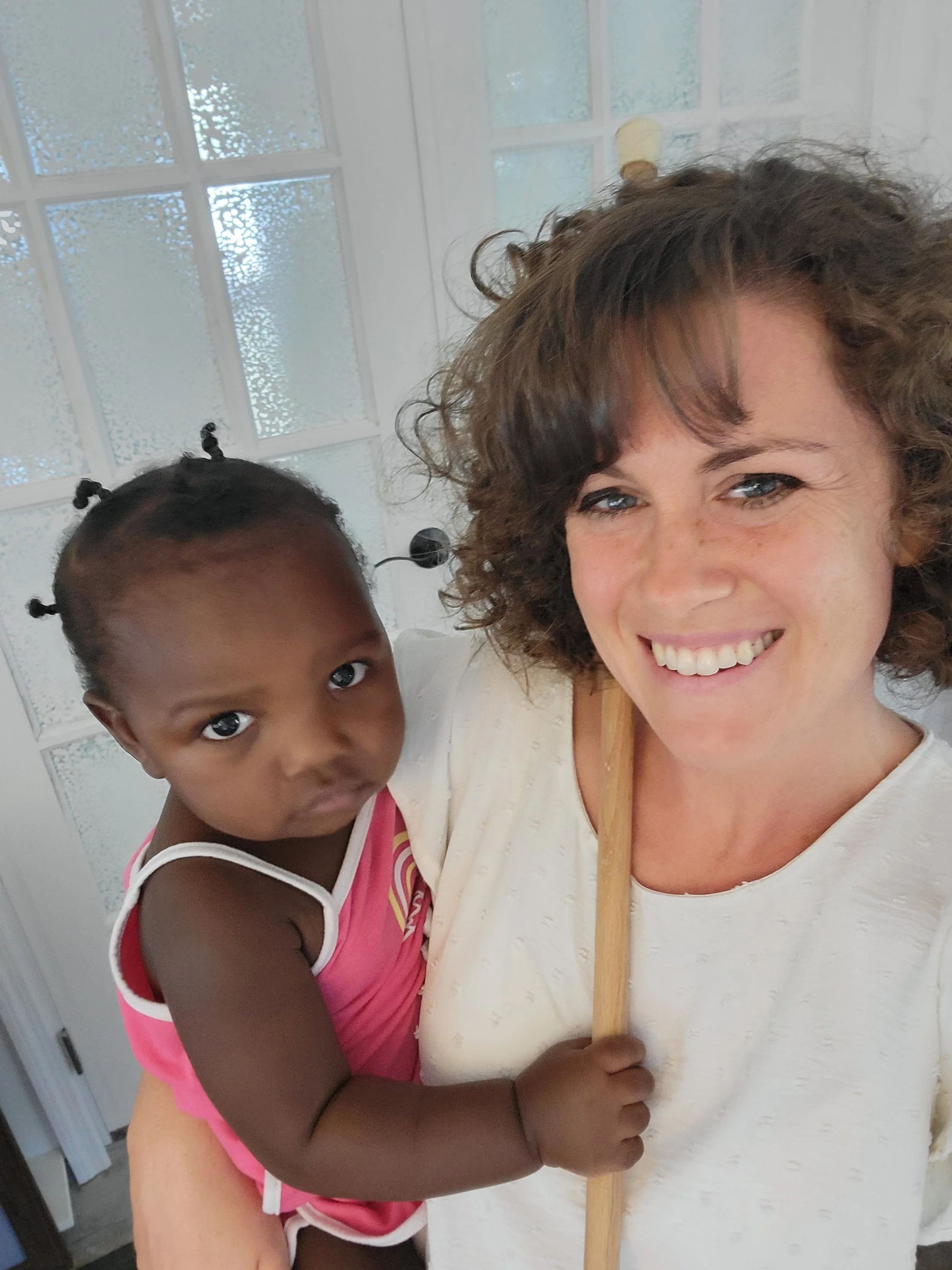 Best JAX newborn photographer holding an african american baby wearing a pink outfit in front of a glass door for milestone cake smash photo shoot.
