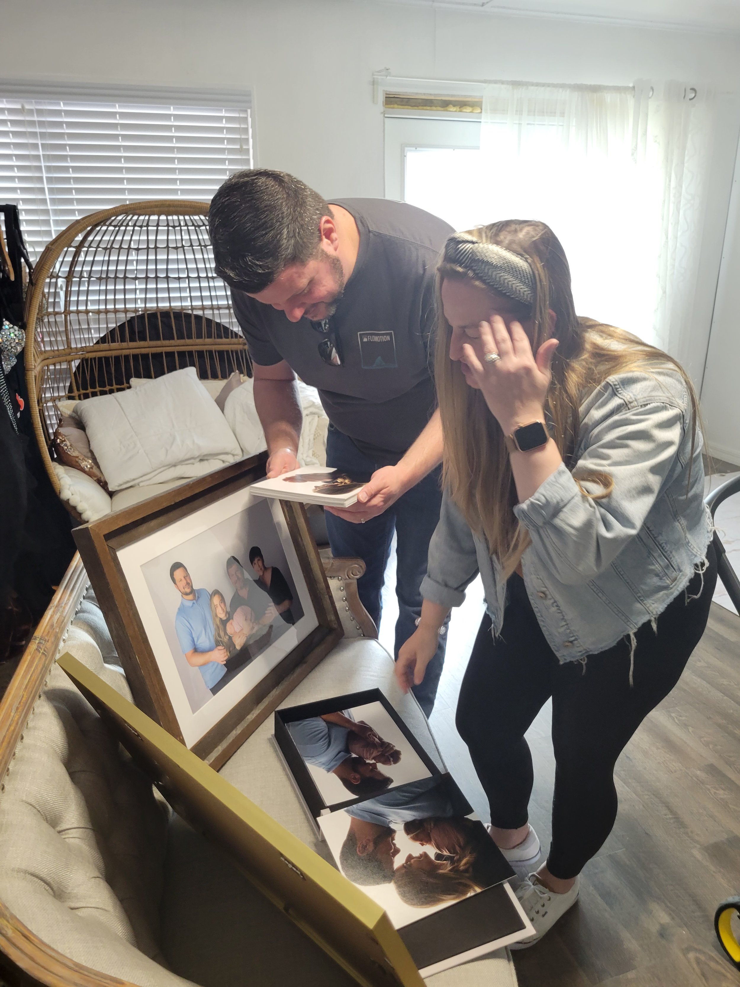 Two people looking at family photos on a couch with framed pictures of their newborn baby girl in St. Augustine FL portrait studio.