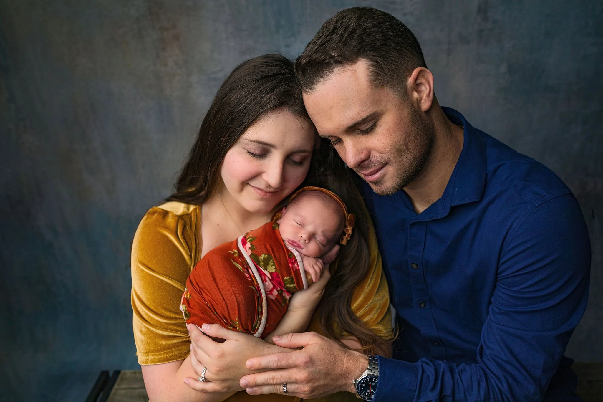 Newborn photography in St. Augustine, FL with family in portrait studio wearing earth tones and fall colors like gold, rust, and navy with baby girl in wrap