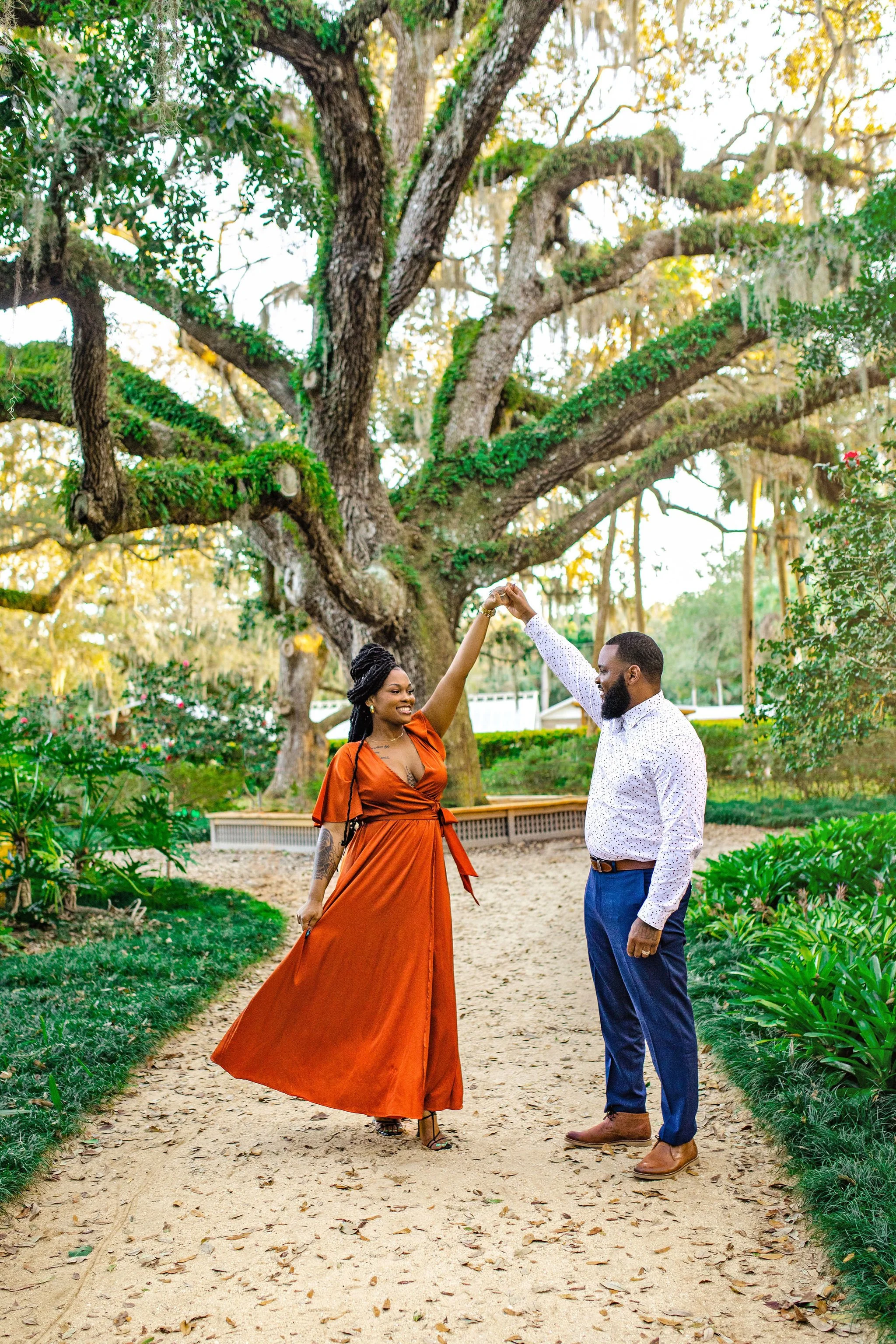 African American family with best photographer in Palm Coast at Washington Oaks Park in front of giant oak tree wearing suit and rust colored dress while dancing