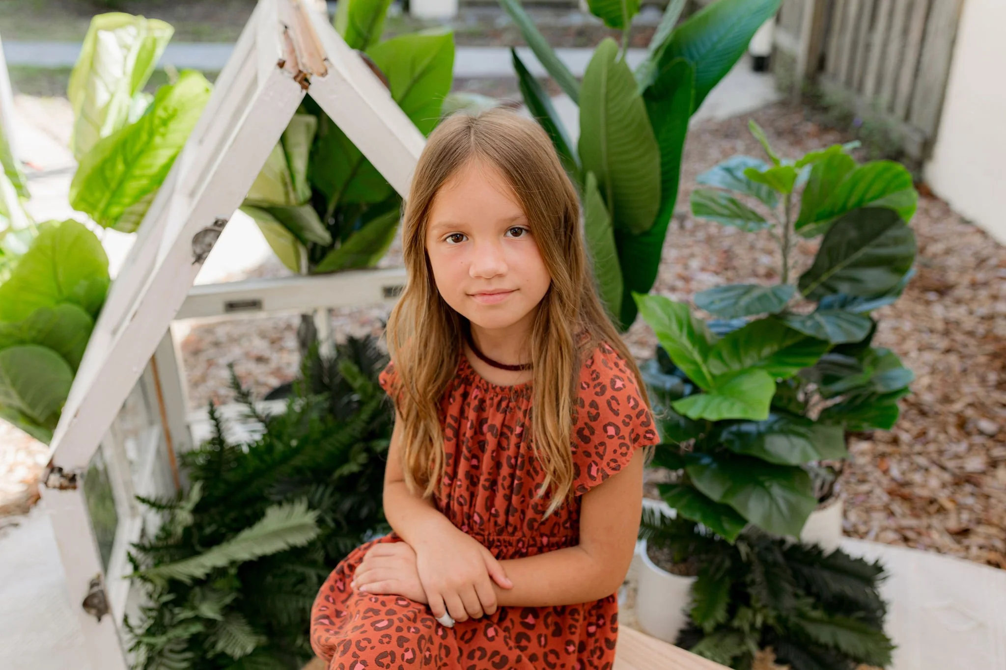 Portraits in JAX photo studio with top family photographer. Young girl sitting among green plants wearing a red leopard print dress.
