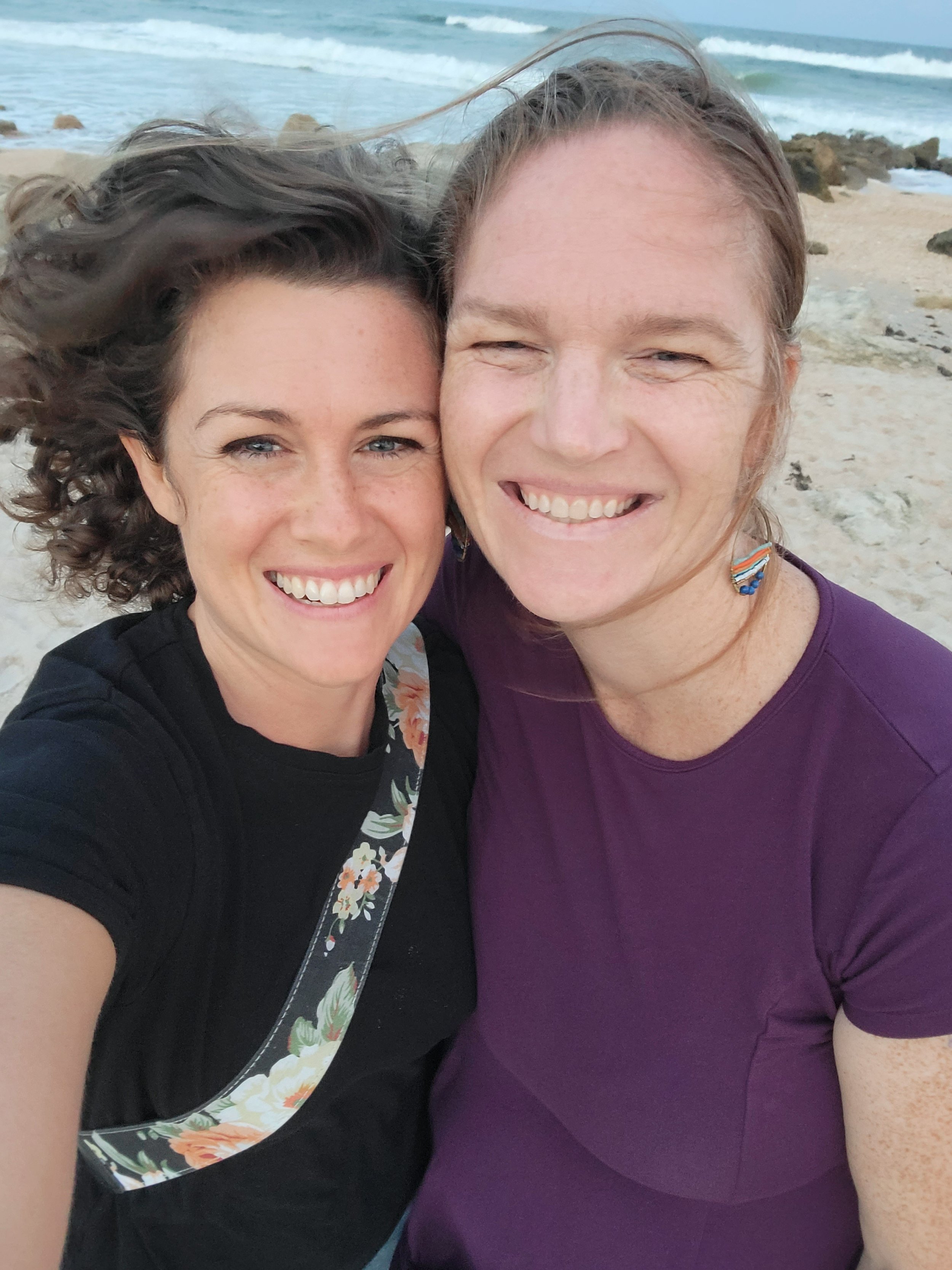 Photographer and pregnant mom smiling on a beach in Jacksonville, FL with waves in the background.