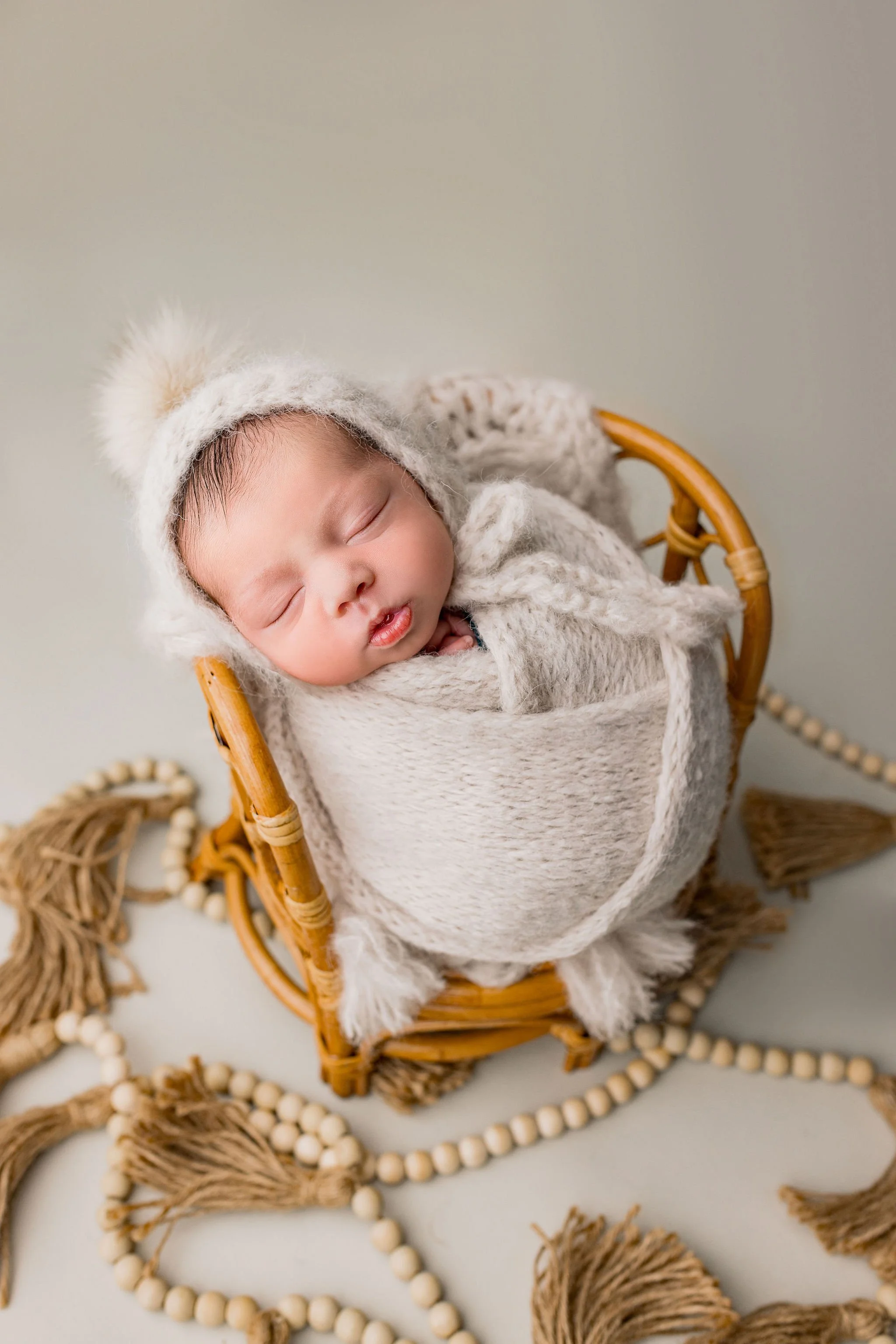 Boho props with neutral background of newborn baby in beige wrap and hat during newborn photography session in Saint Augustine, Florida