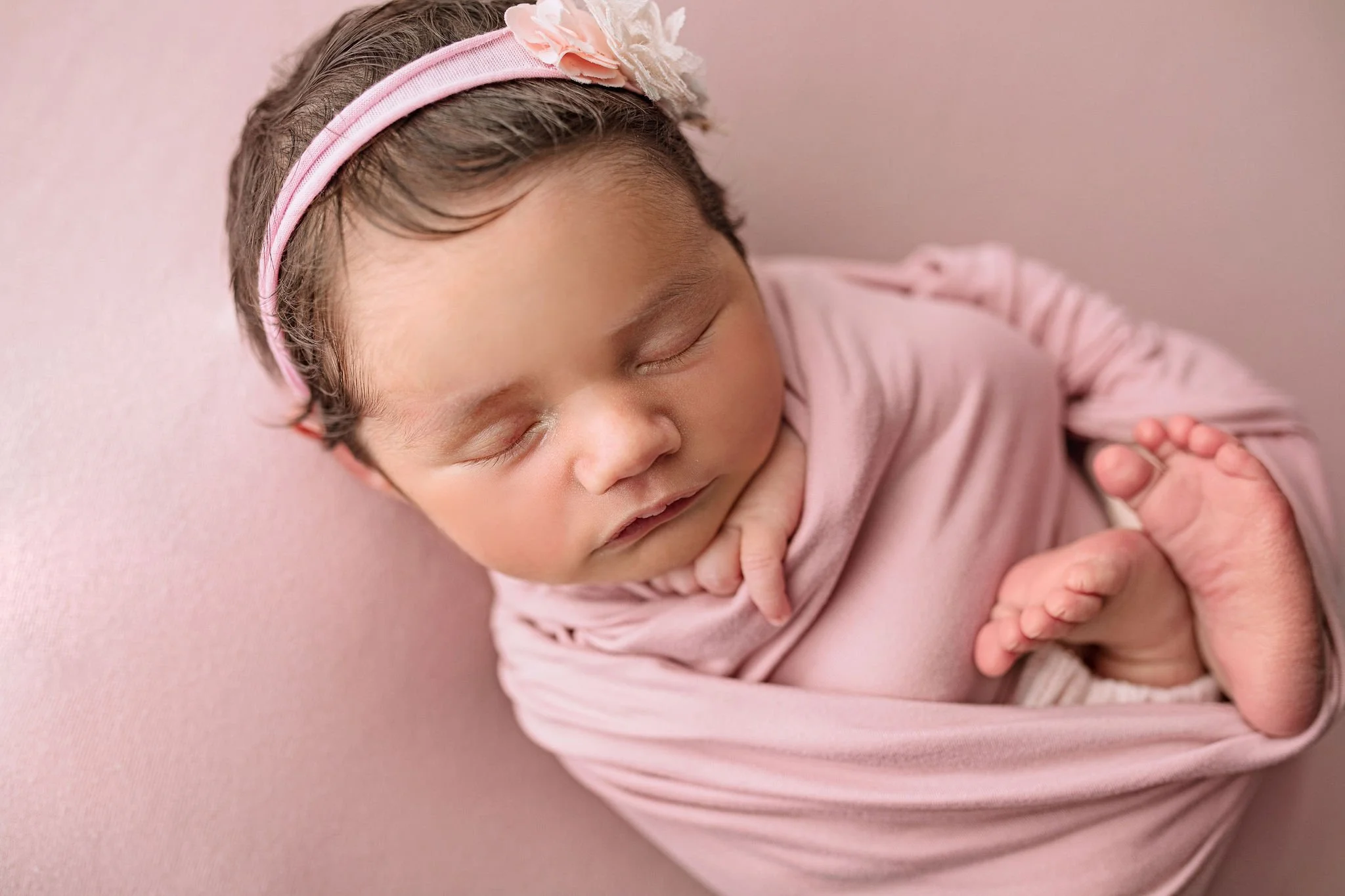 St. Augustine, FL newborn photography with baby girl in soft pastel pink wrap and background in simple pose after IVF pregnancy