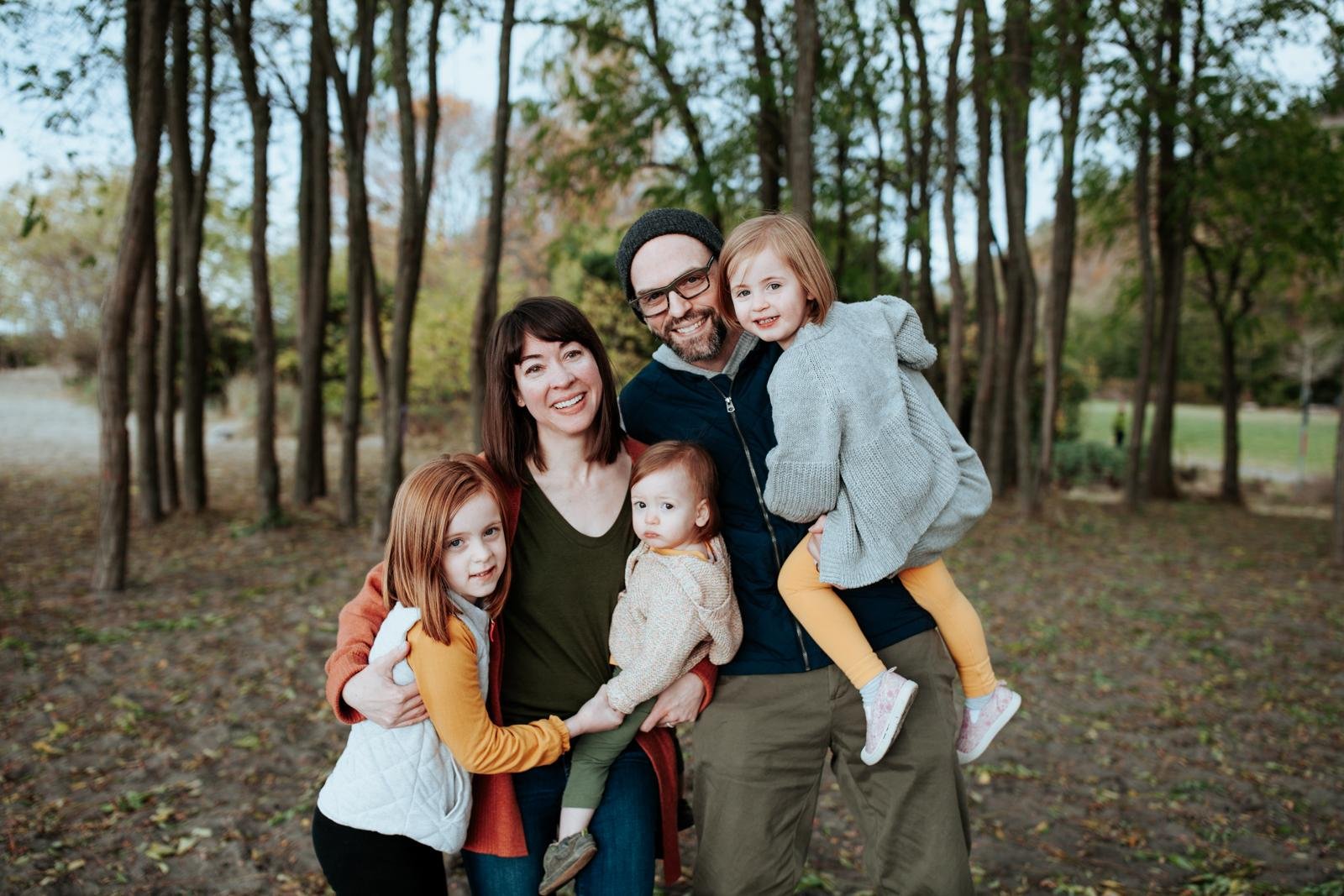  A family hugs and smiles in a tree grove for a candid family portrait at the best fall mini sessions in Seattle.&nbsp; 