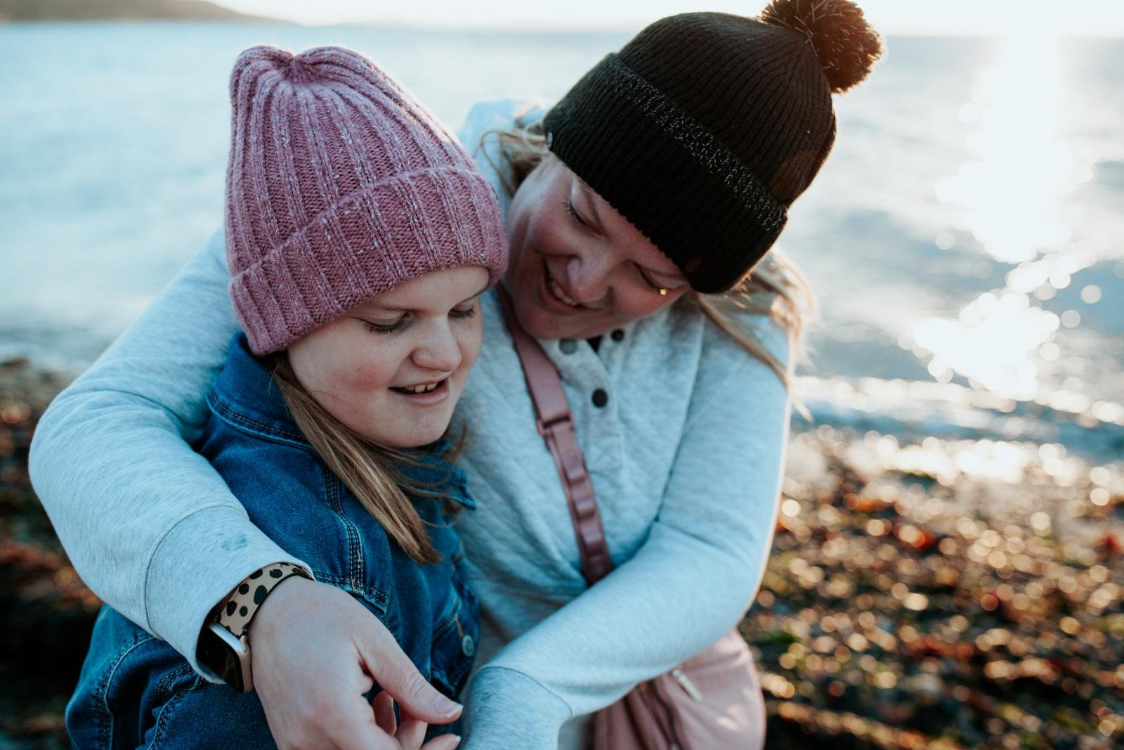  A mom in a winter hat hugs her daughter on the beach for lifestyle fall mini sessions on Golden Gardens in Seattle.&nbsp; 