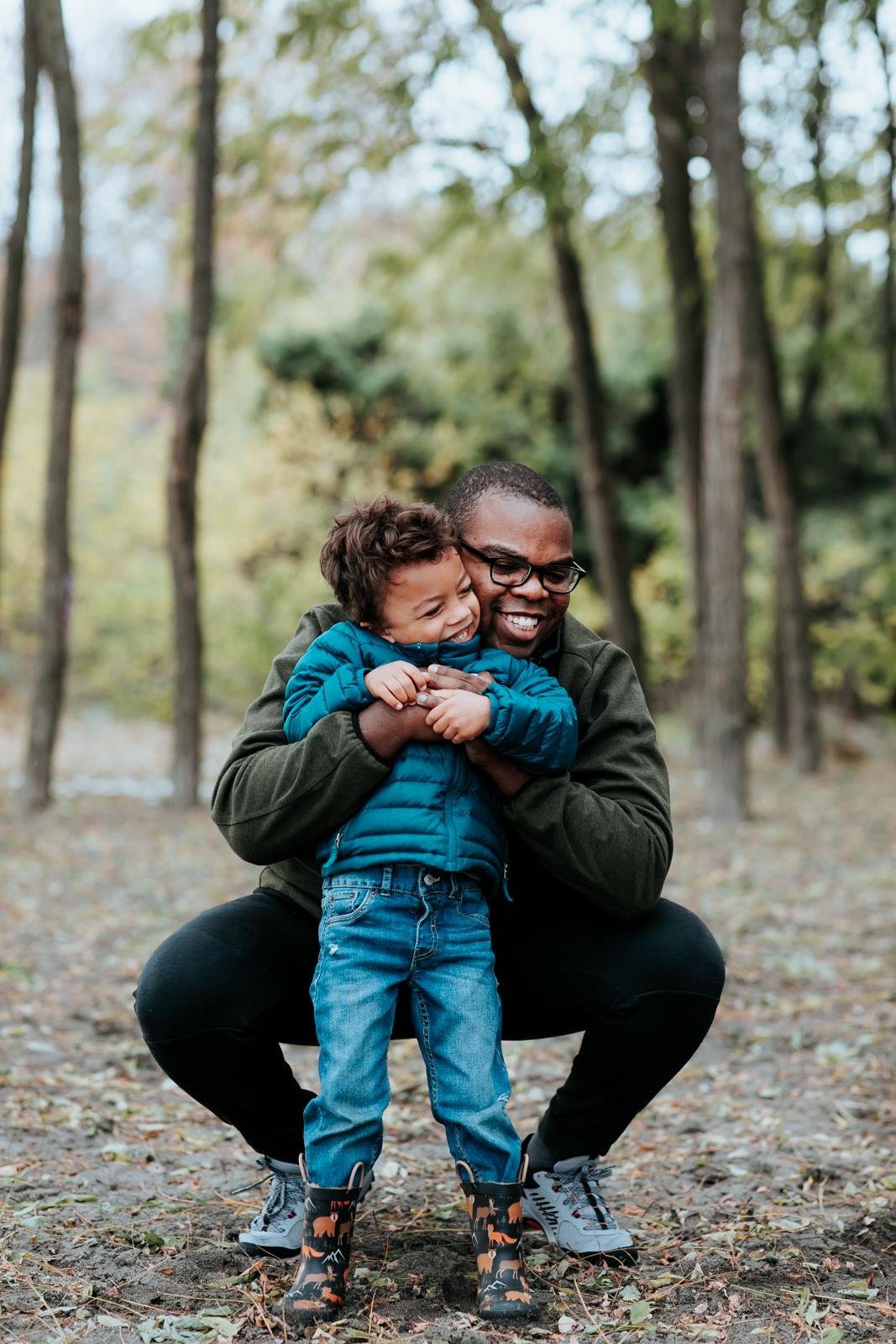  A boy in a blue coat gets a big hug from his dad in a tree grove for a candid family portrait at the best fall mini sessions in Seattle.&nbsp; 