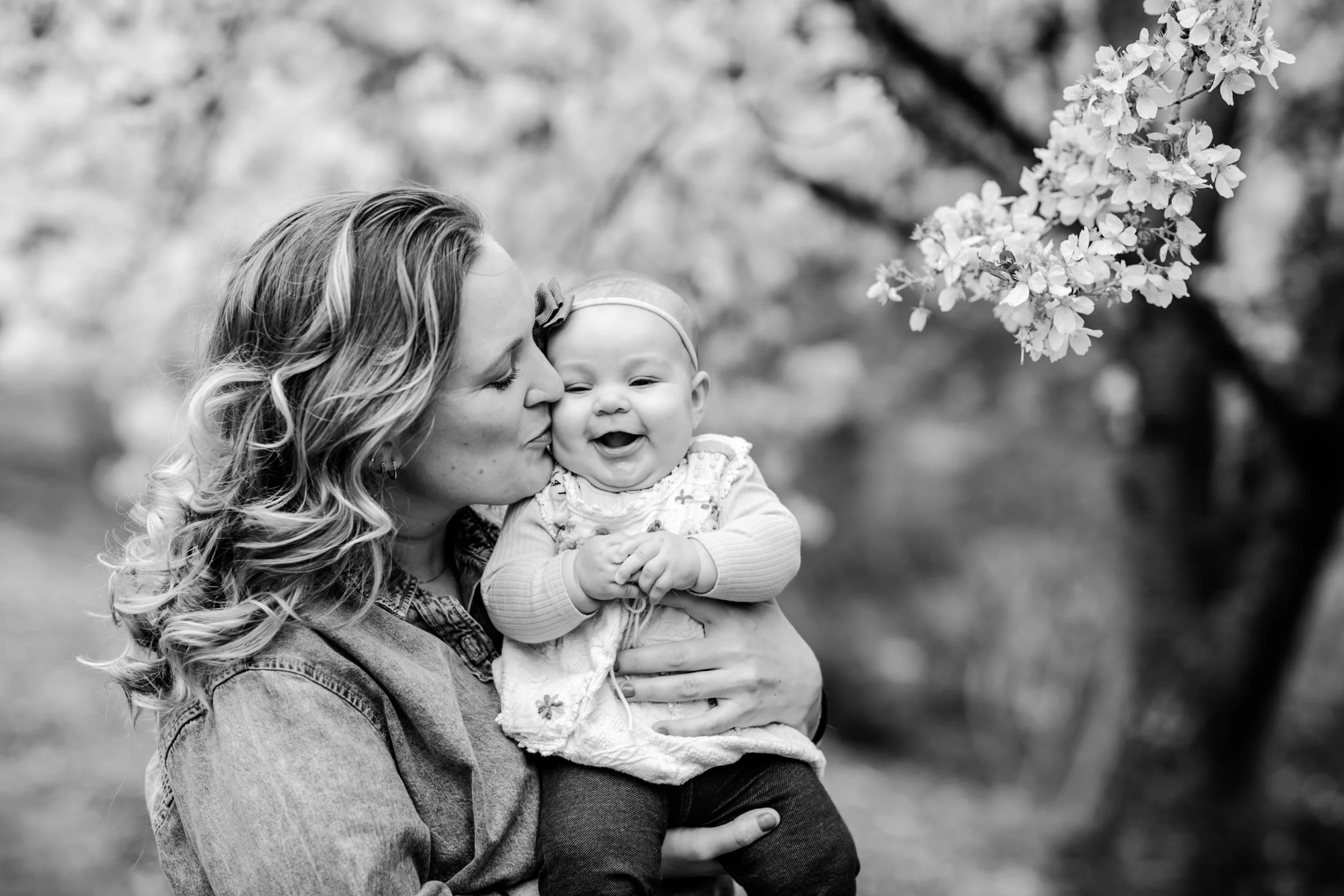 a mom kisses her baby girl under a cherry blossom tree