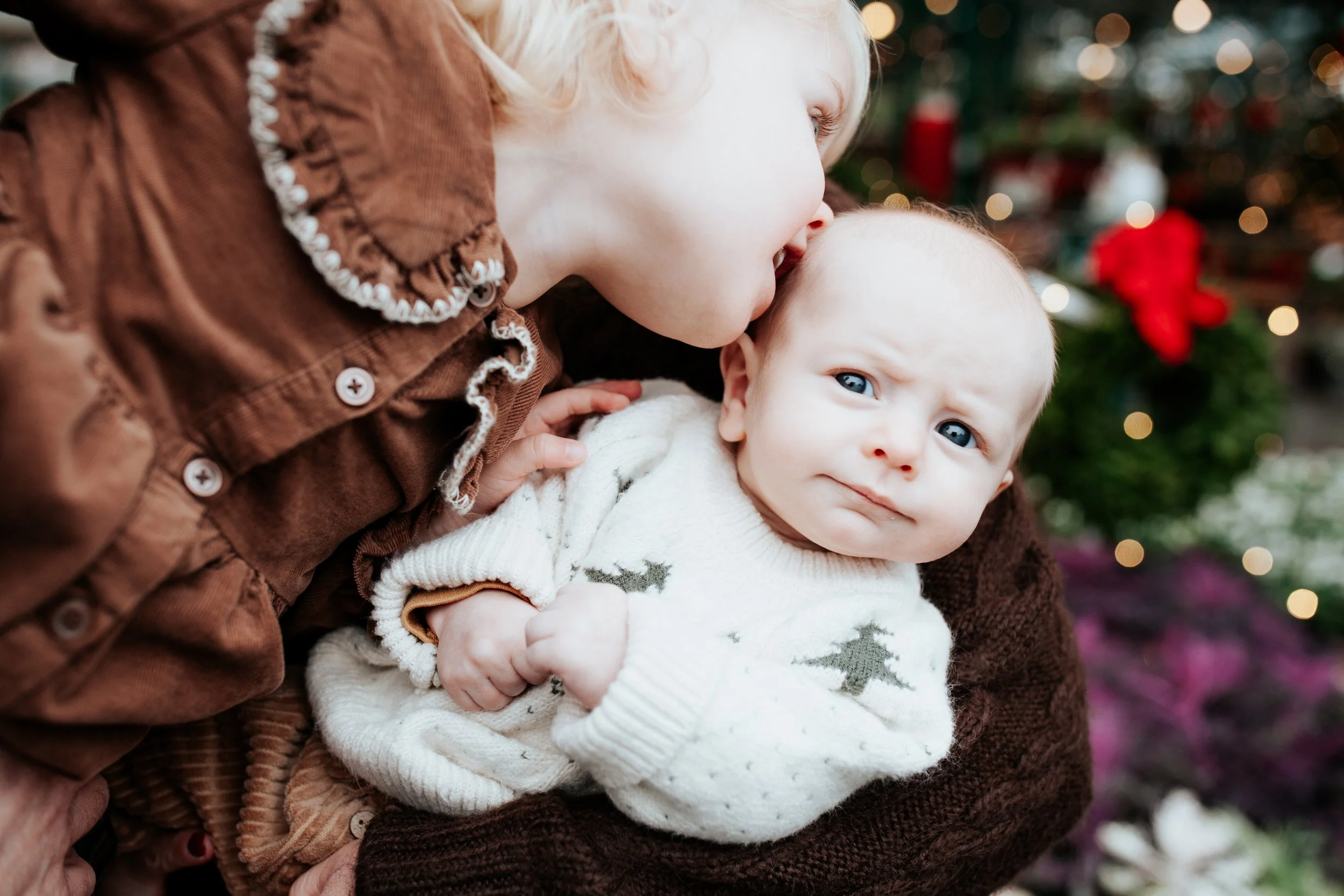 a girl gives her baby brother a kiss for holiday photos