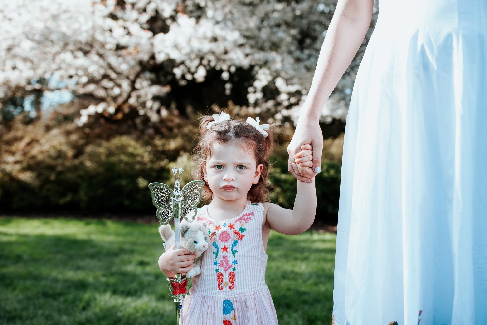 a girl holds her mom's hand under a cherry blossom in the spring