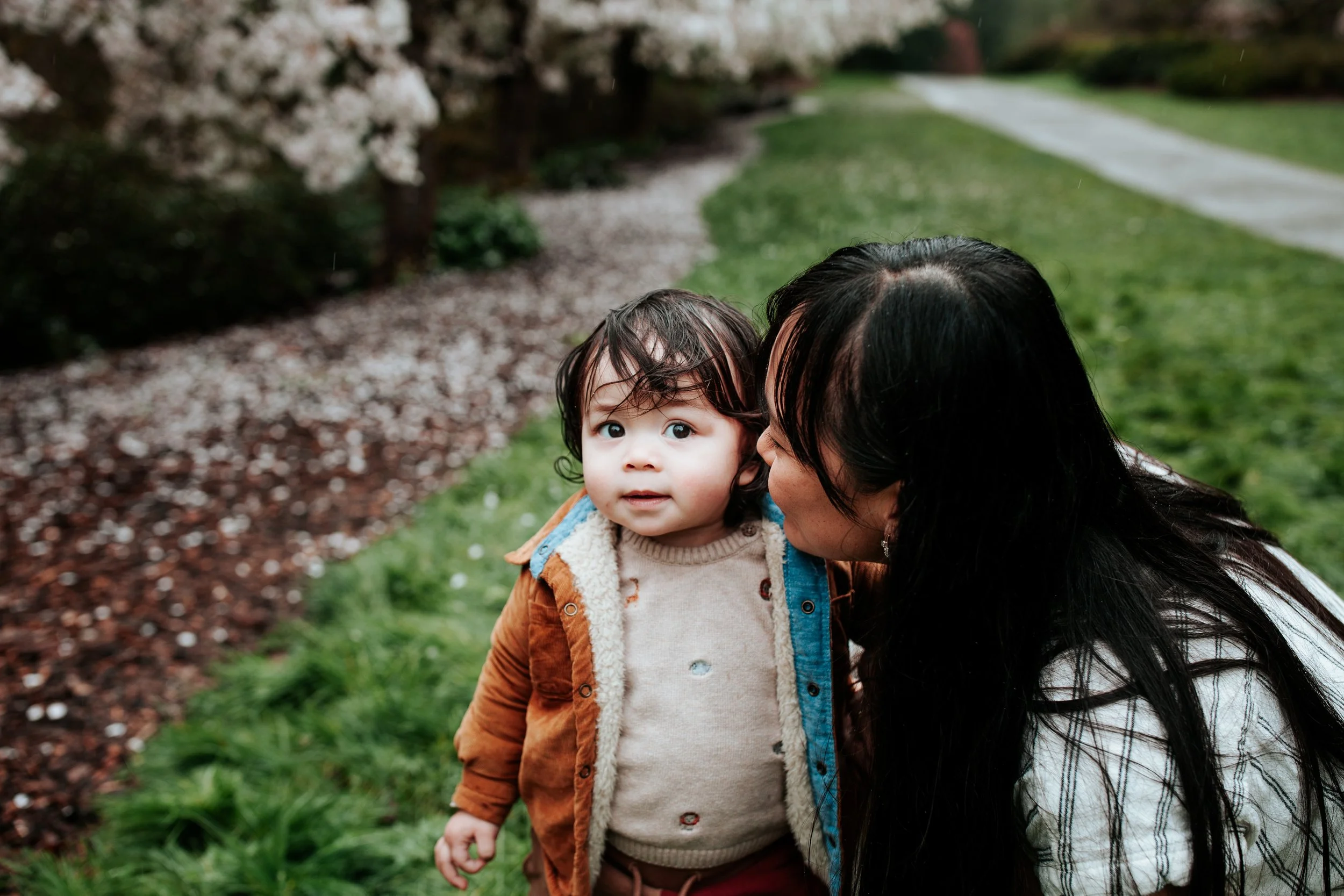 a mom kisses her son under the cherry blossoms