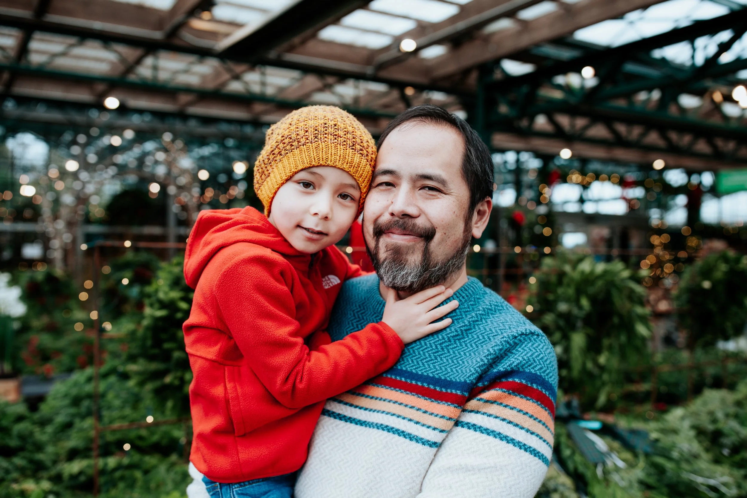a boy in red hugs his dad for holiday tree farm photos