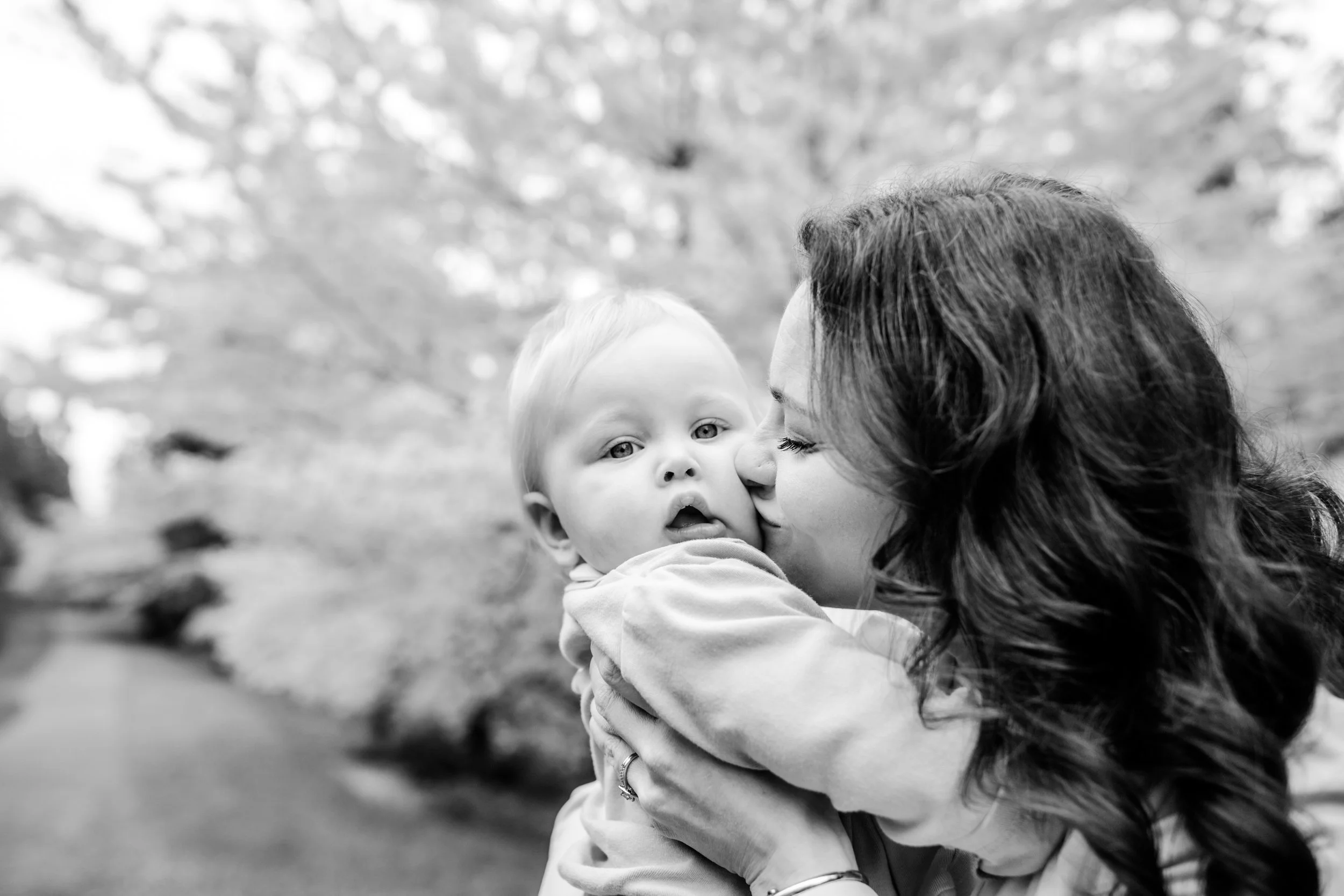 black and white photography of a mom kissing her baby under a cherry blossom