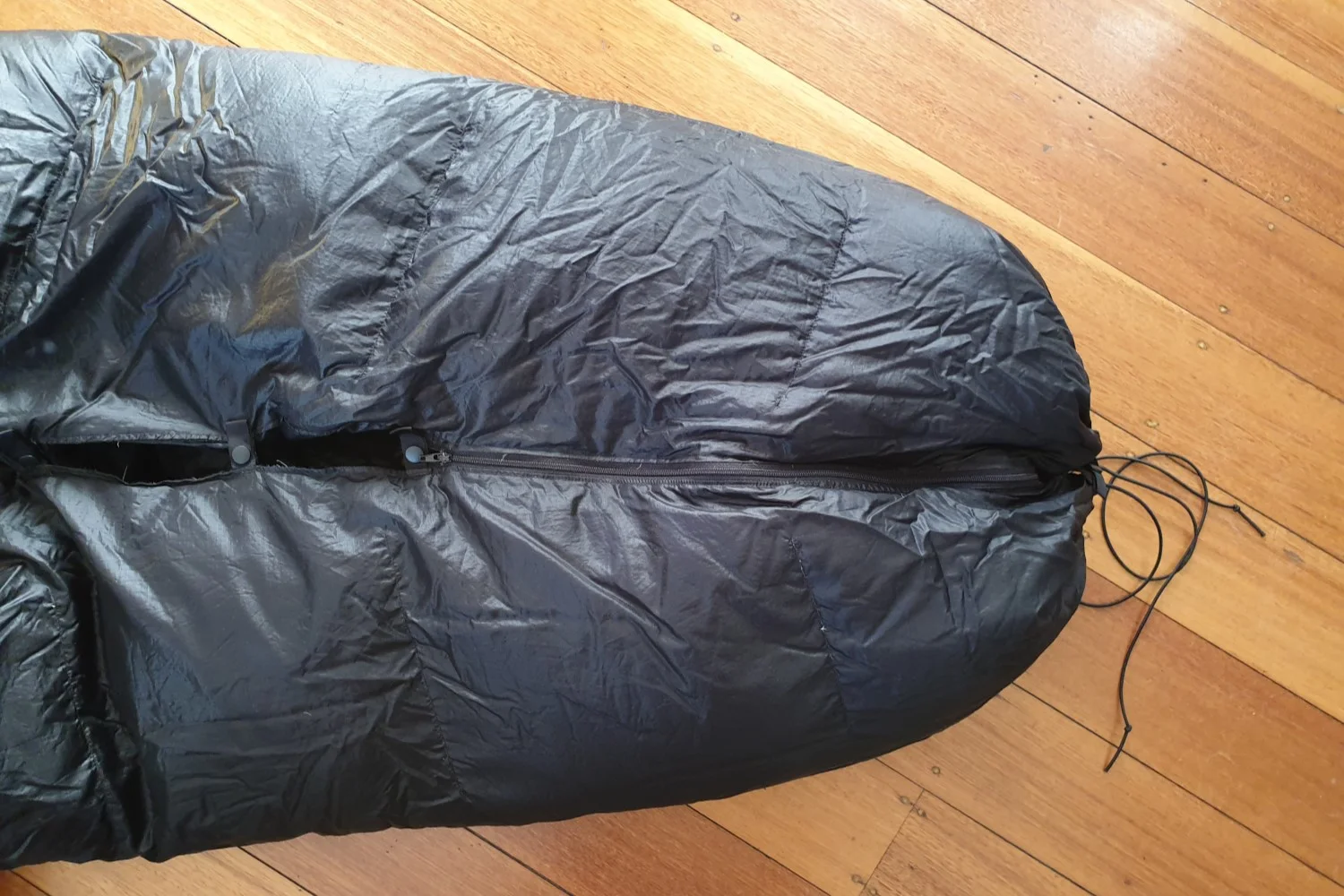 Example of a zippered footbox, as found on the Enlightened Equipment Revelation. In the middle you can see the short zip, on the left you can see several button clips for fastening the remainder of the lower half of the bag, on the right you can see the drawstring for cinching in the bottom of the bag once the zip is done up.