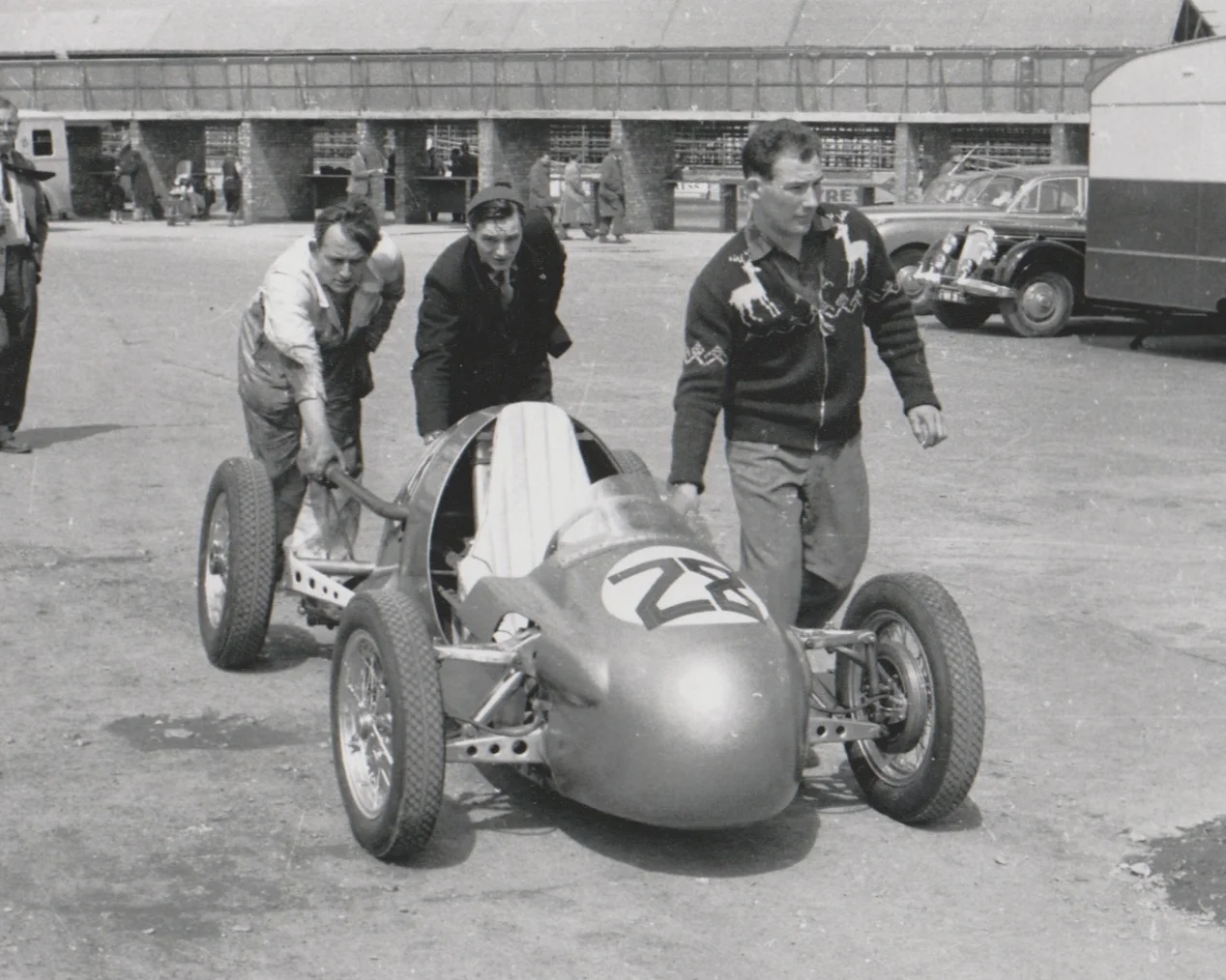 Stirling Moss proudly walks along with his new works F3 Kieft 500 single seat race car.