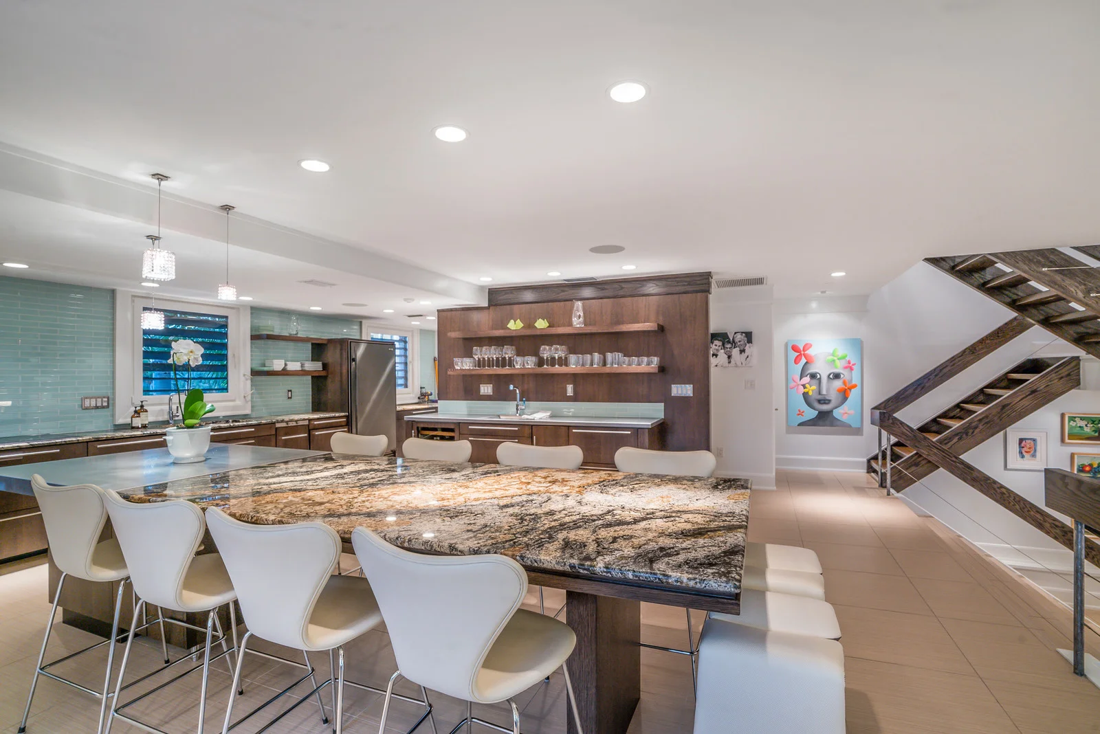 Another glance shows us the second half of the main living space, a chic kitchen and entertaining space, complete with wet bar, granite and stainless counters, and built-in dining space. Glass subway tiles and floating wood shelving make this mid-century-inspired kitchen au courant.