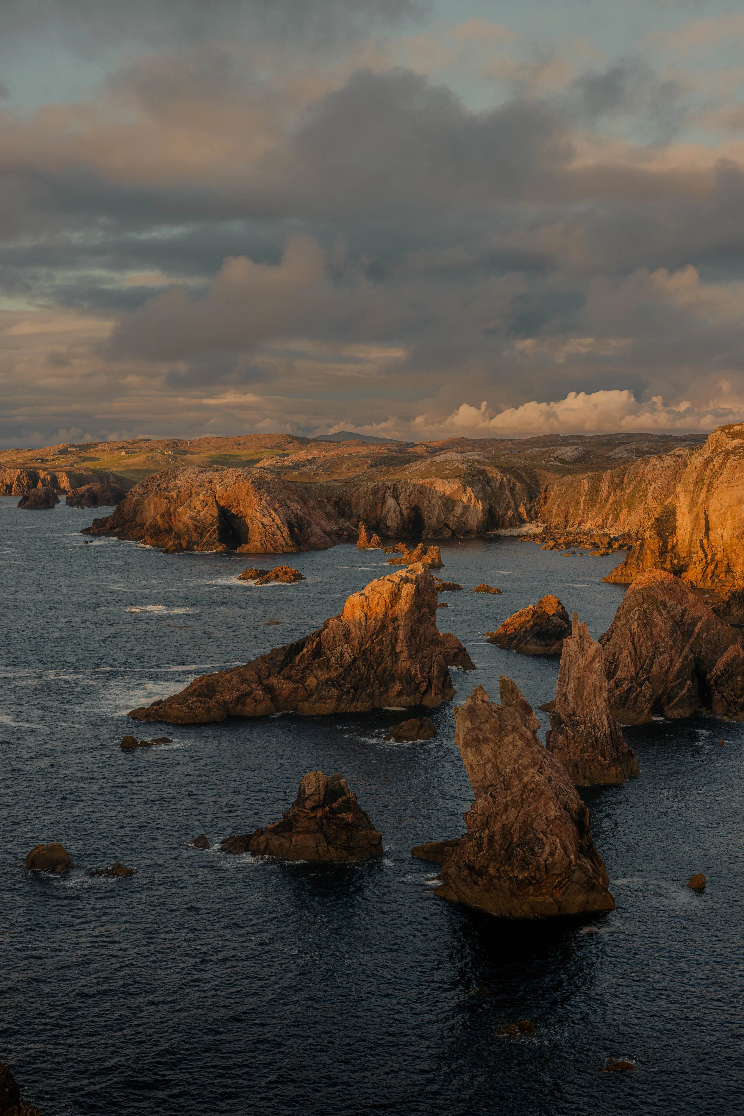 Rugged sea stacks at Mangersta, Isle of Lewis, Scotland. The golden sun light is illuminating the rock faces as the waves crash below