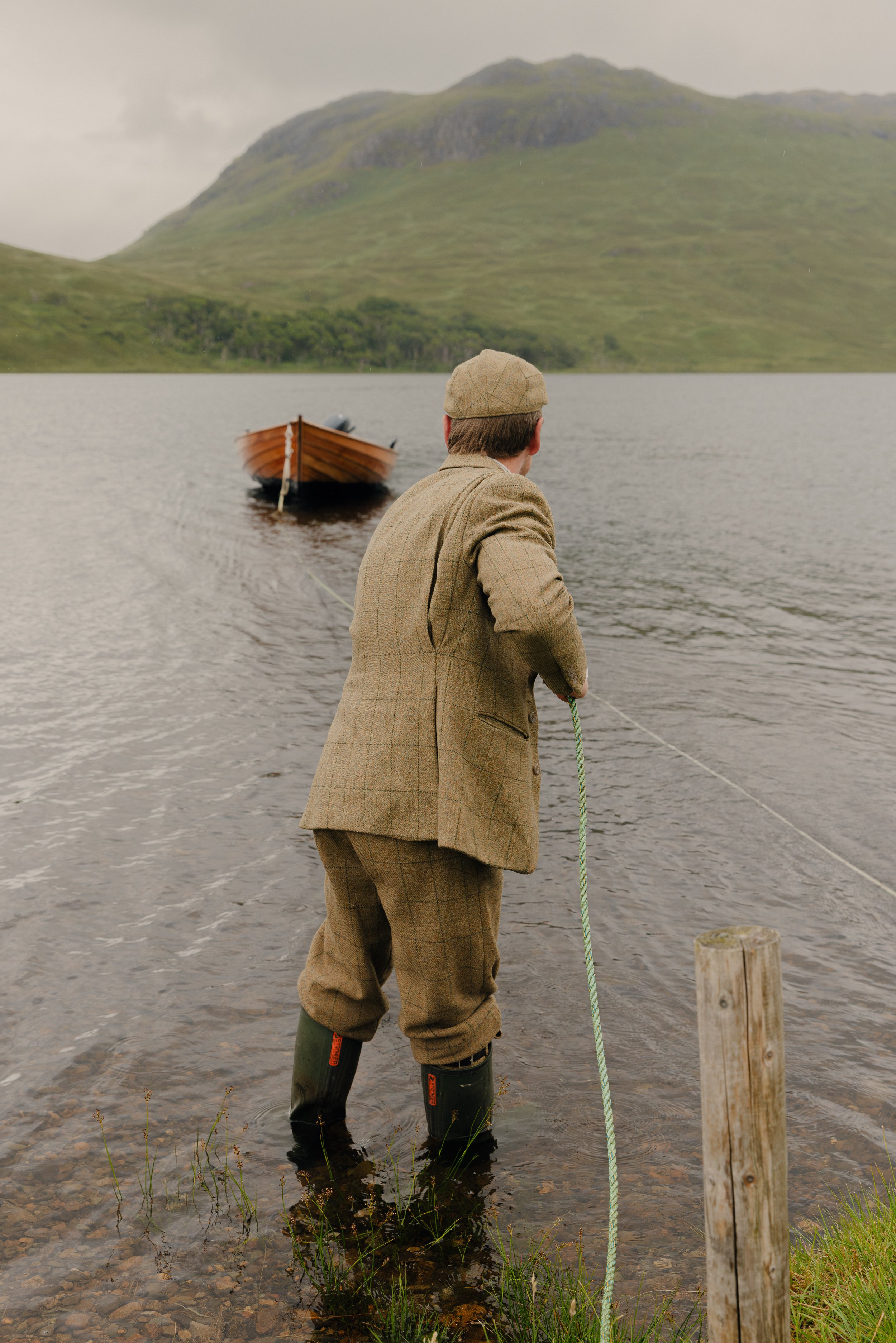Ghillie in full tweed pulling in a wooden boat on a Loch in the Scottish Highlands