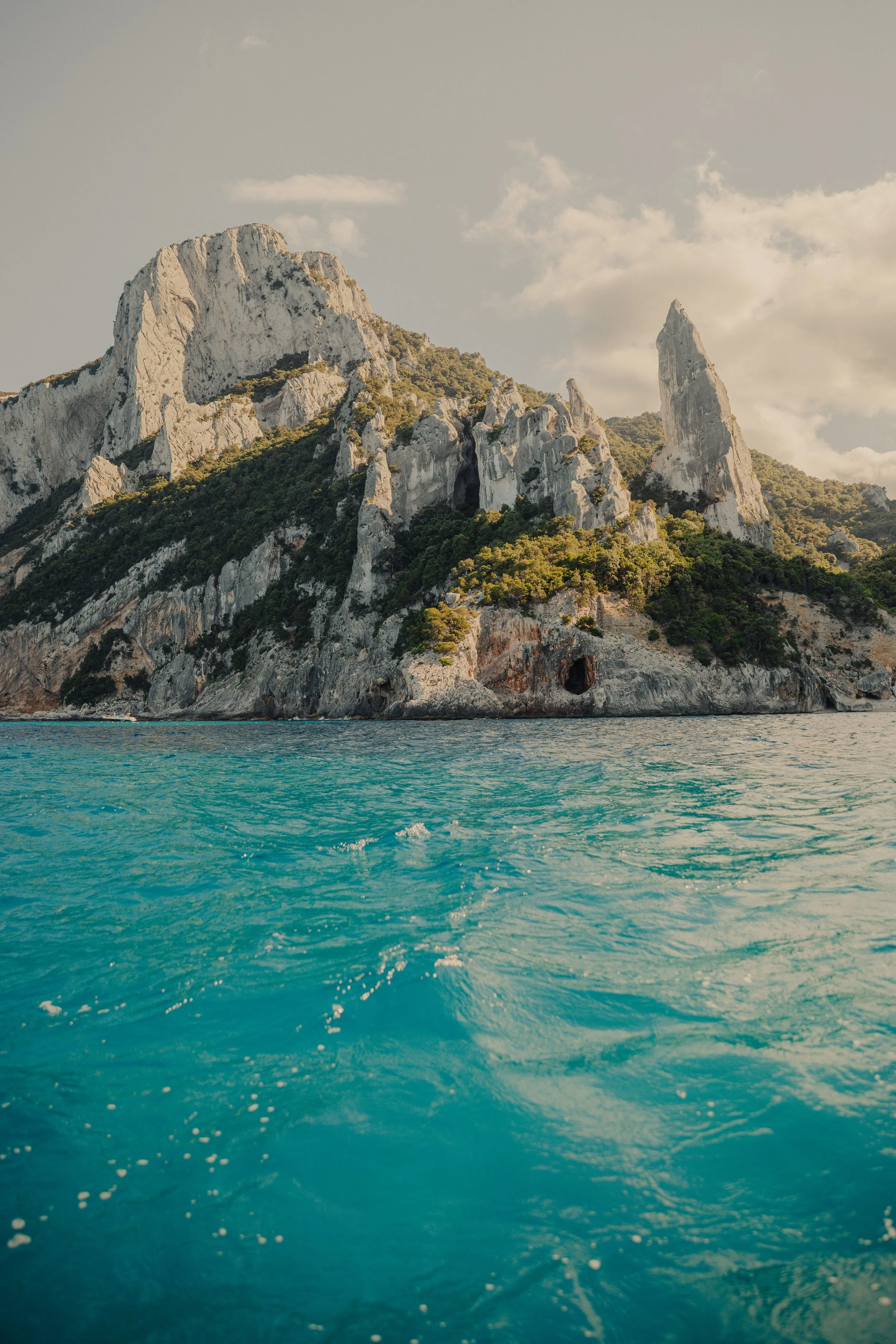A striking limestone sea stack and jagged cliffs rising from turquoise waters at Cala Goloritzé, Sardinia