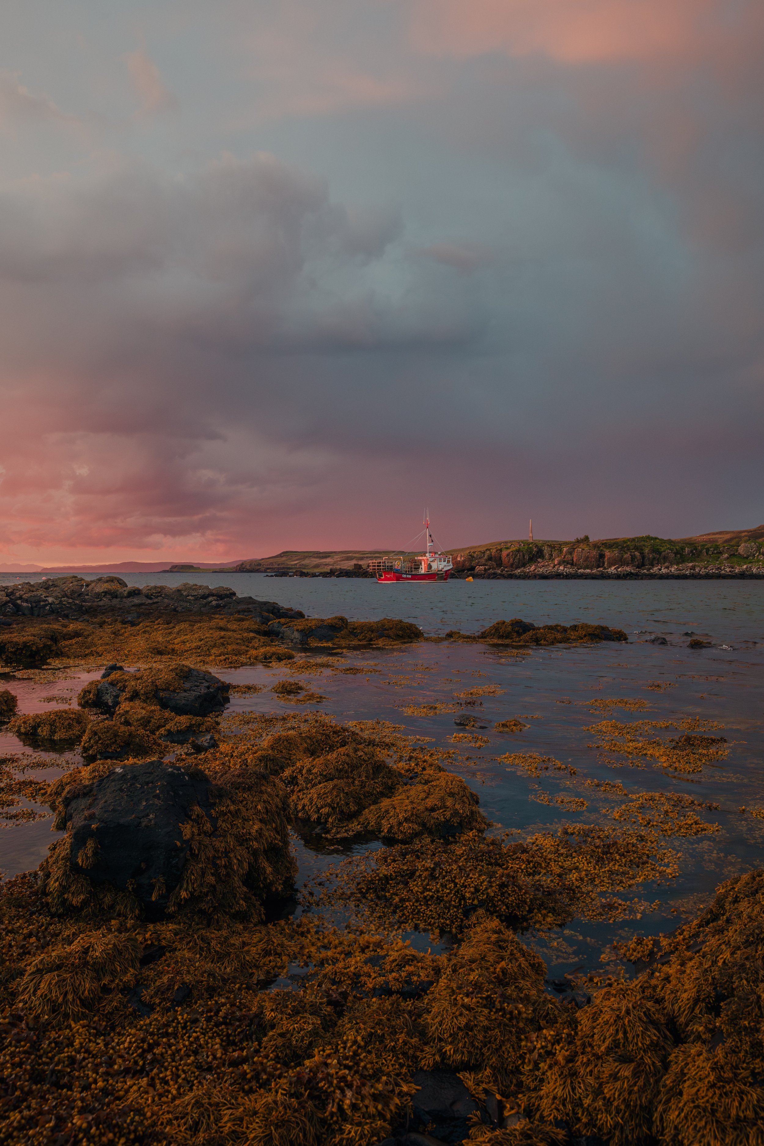 A creel boat sits in a quiet harbour on the Scottish west coast during a firey sunset in summer