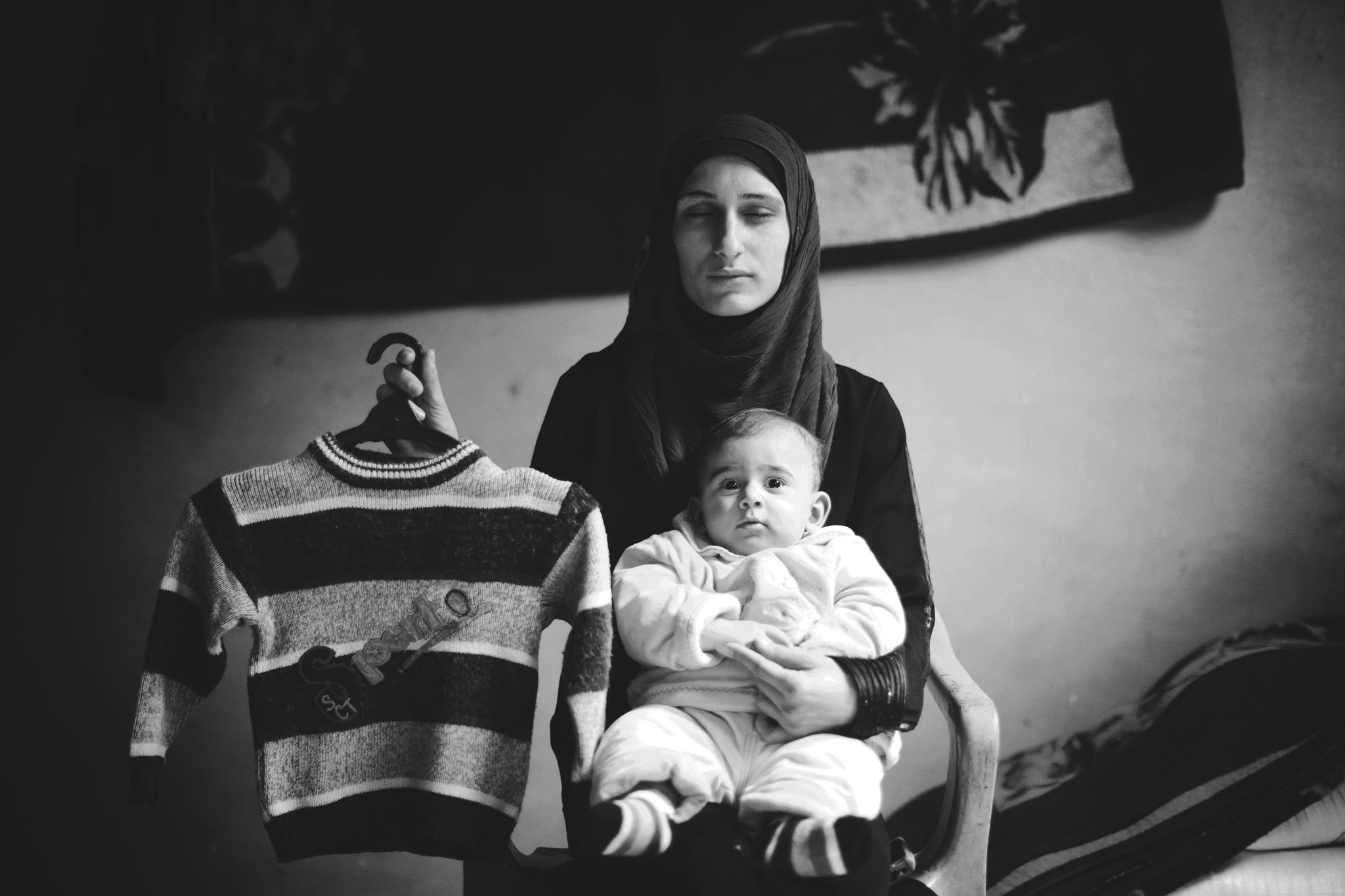 "nothing replaces a son,not even another son." Safia Abo Zour, 25 years old, holds her five-month-old baby (Mohammed) with one hand. In her other, she displays the shirt that her older son, Mohammed, aged-4, wore the last time he went to kindergarten. Mohammed had just turned four years old when he was killed during the second war in Gaza, 2011, after an airstrike targeted his family's house in the Al Zaitoun neighborhood. Safia named her new baby "Mohammed", in memory of his brother. © Images by Eman Mohammed | Broken Souvenirs series.