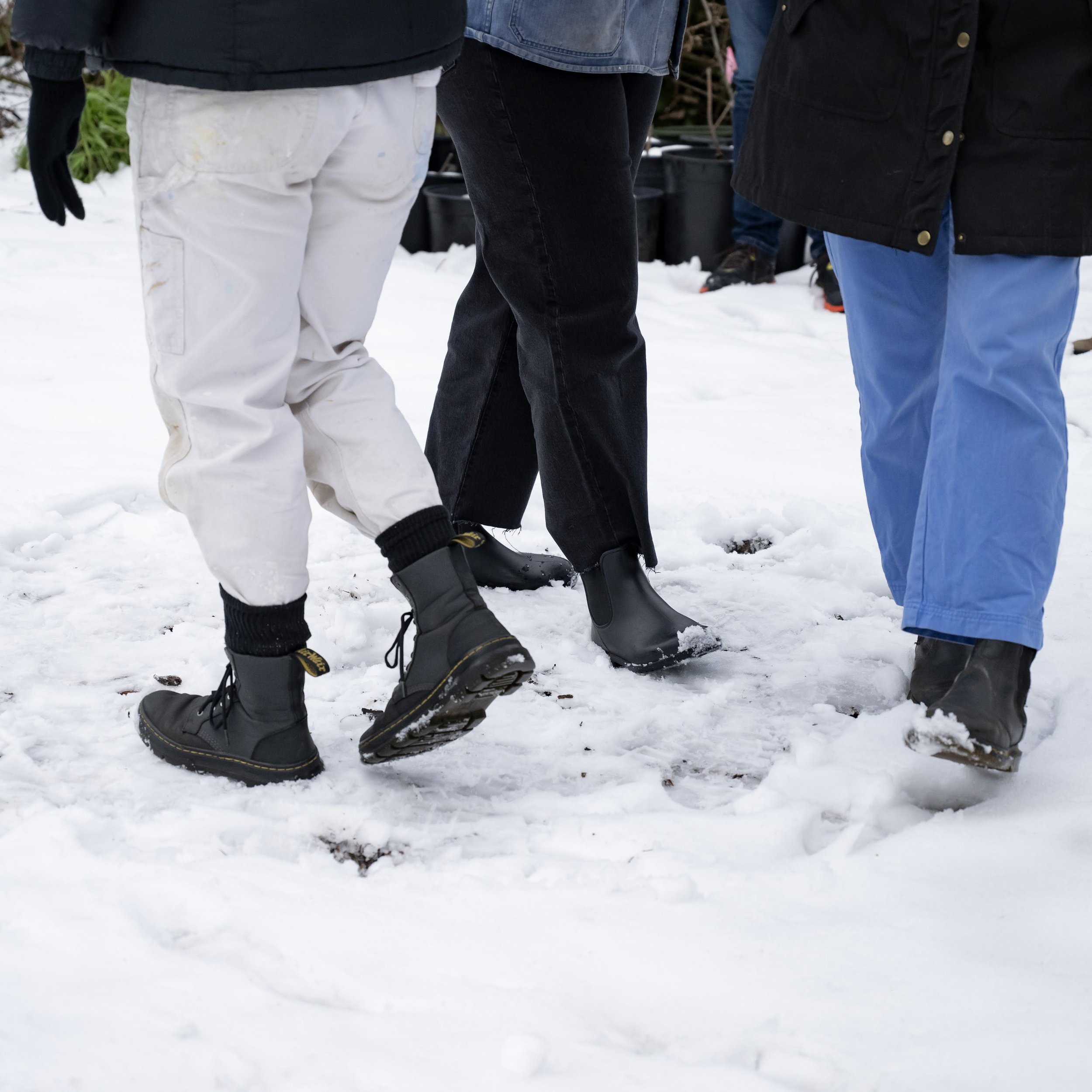  three peoples legs: they are all wearing pants and boots, and they are walking in a circular formation in the snow  