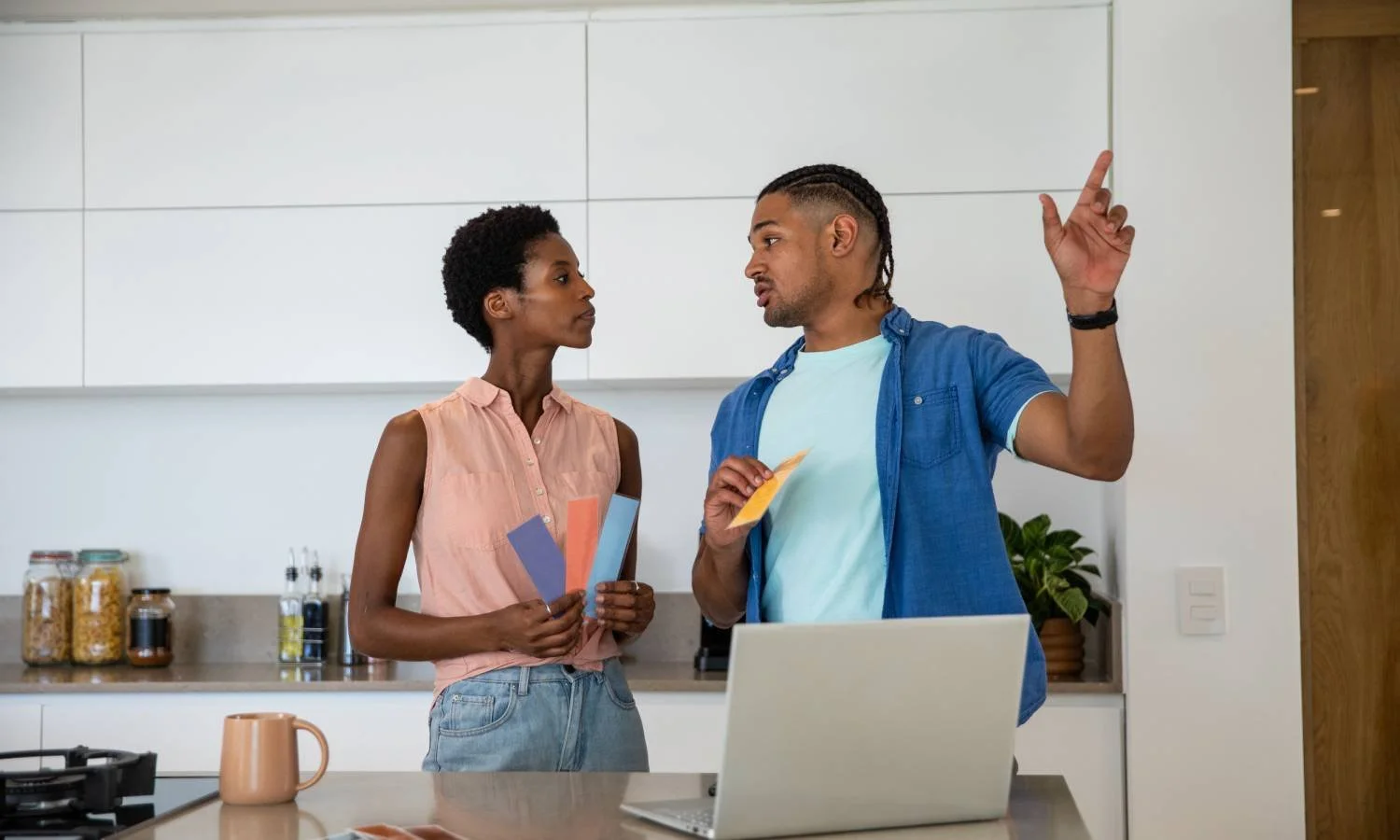 Couple in a kitchen holding vertical paint swatches and discussing the best option for their space