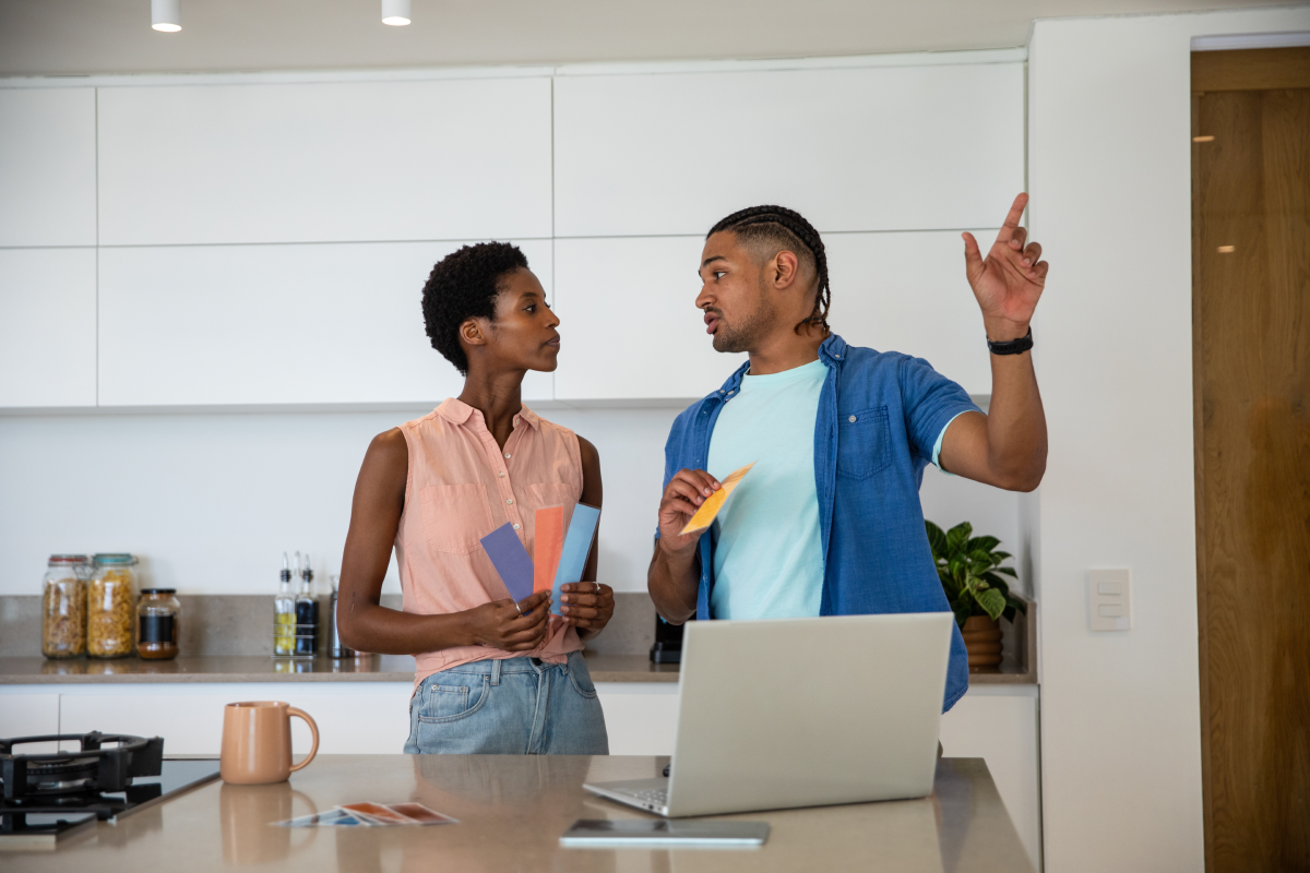 Couple in a kitchen holding vertical paint swatches and discussing the best option for their space