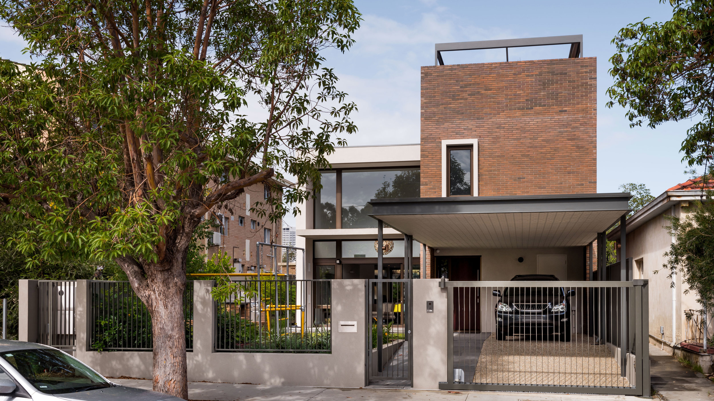 Carr Plc. We aimed to create a home which responded to its context but also maintained the privacy and internal separation required by a young family. The styling is dark and modern with an honesty of materials and spaces. Lighting is moody and soft complementing the home without oversaturating the spaces. The design uses warm materials that respond to the semi-industrial context of the street. Textured face brick is celebrated through-out the design to bring earthy rawness to the internal spaces. A perforated Breezewall separates the entry space from the living spaces while still maintaining a filtered visual connection between the two. The context has also influenced the location the outdoor and living spaces allowing them to feel connected to the street, without sacrificing privacy and amenity. Landscaping and automated drapes add layers of separation for these spaces and allow the users to moderate their connection with this busy social street.