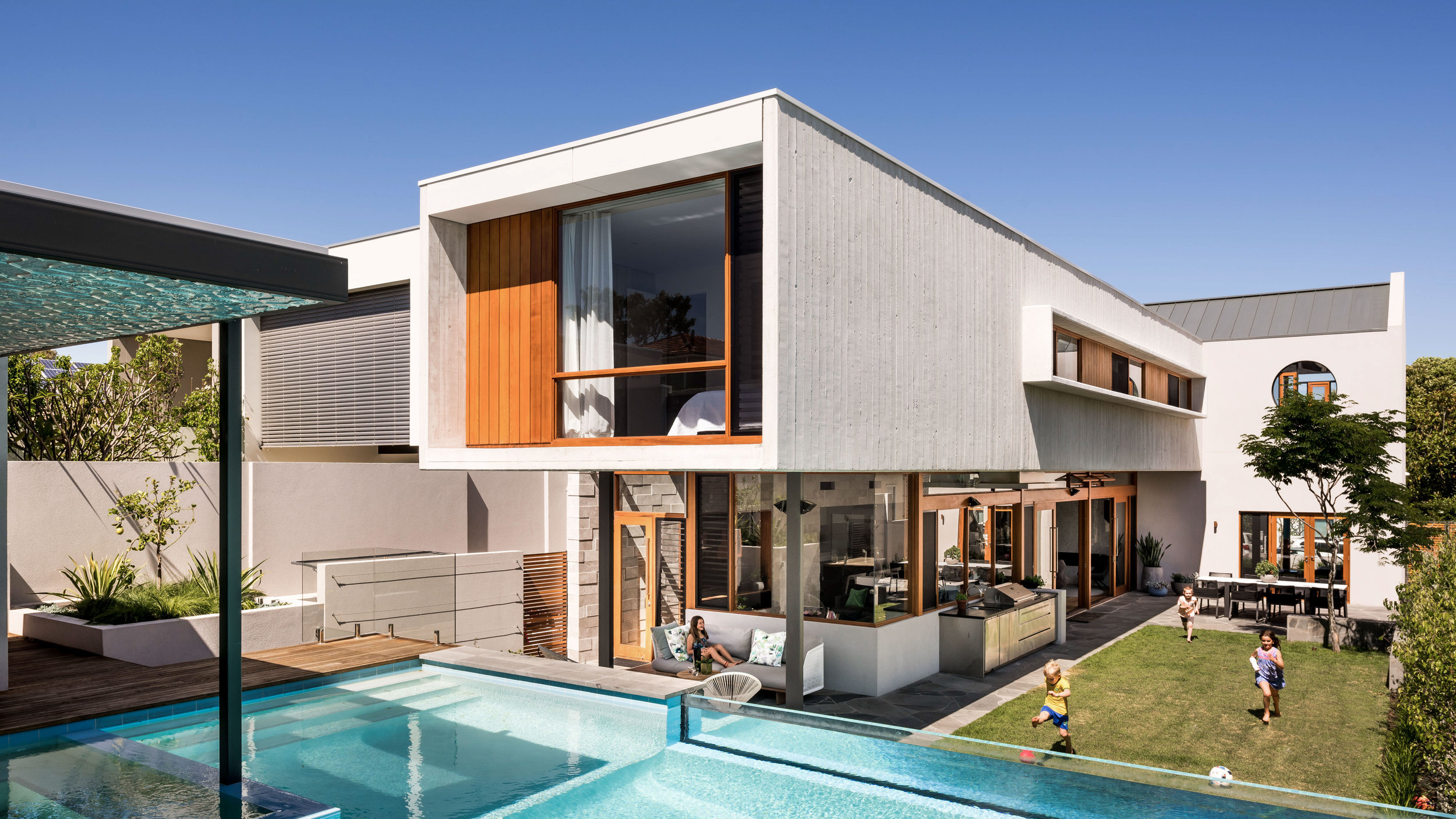 St Leonards Ave. This home explores interconnected spaces, materials and volumes. A young family with interconnecting lives set a brief for a robust family home. Large open living spaces, connection to outdoor areas as well as private living and playing spaces are all elements of an intricate brief. A building form developed that celebrated two distinct design directions in a single composition. A strong curved form of stone creates arcs through the home, opening up to the street to form an entry and to the rear to access the backyard, swelling in the centre to conceals the machine of the house. Small bridges take you through penetrations through this thin skin to servicing side. Partnered with this curve is a massive concrete box which floats over the living spaces providing an eave to the North glass forming a veranda. This form contrast the curve and strengthens the impact through their interrelationship.
