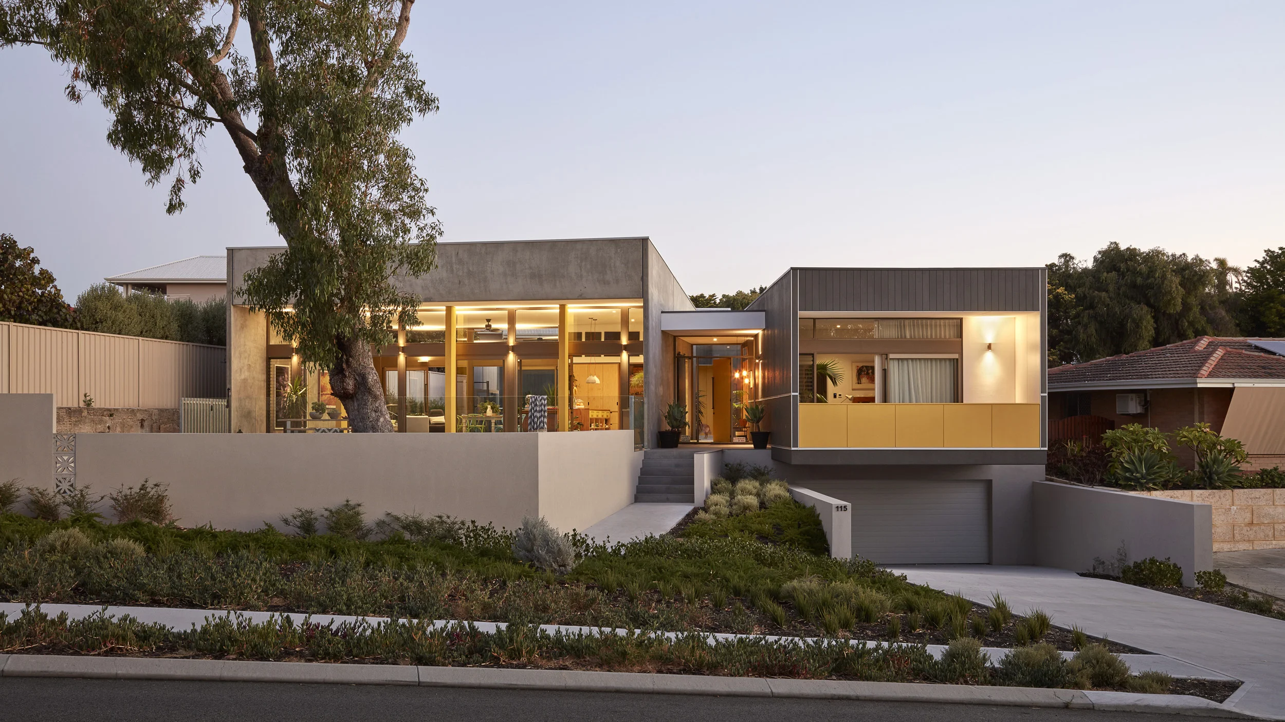 Elliot Rd. This home challenges notions of a coastal suburban home. The external living spaces are in the front yard, not concealed from the neighbours. The main living room references the soft blue glow of a suburban night and appears from the street as a frame, like those illuminated blue boxes adjacent. This room has no TV. The home creates an internal protected courtyard to provide an external space sheltered from afternoon breezes. The house wraps and engulfs this courtyard with a series of connected spaced opening onto it. Raw concrete responds to a beach aesthetic, while dark painted timber creates a contrast for the sheltered spaces within this form. The two forms are linked by a transparent entry which draws the eye into the internal courtyard. This design presents an architectural exploration of the coastal suburban home pushing the established context.