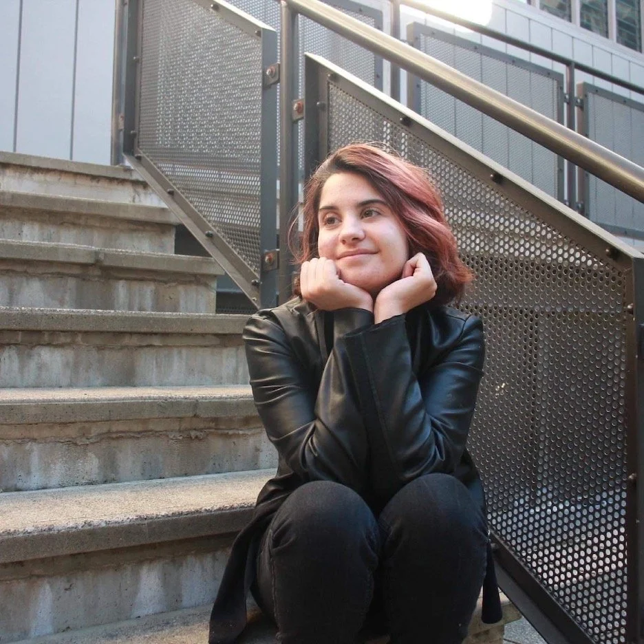 Stephanie wearing a black leather jacket, sitting on the outdoor steps at TAFE
