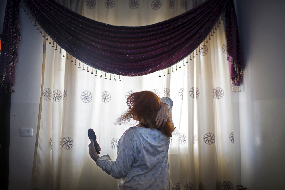 ONCE HER CROWNING GLORY
Poet Hala’s grandmother, 88, brushes her vibrantly dyed hair, once her crowning glory. Her son died fighting in Syria. She had advised him on his wedding night to slap his new wife once, to assert his authority. Despite that abrupt beginning, the marriage had been a happy one until his death. Her granddaughters are respectful but quietly laugh at the elderly woman’s advice about how women should live. She died one year after this photo was made, a Syrian refugee in Jordan.