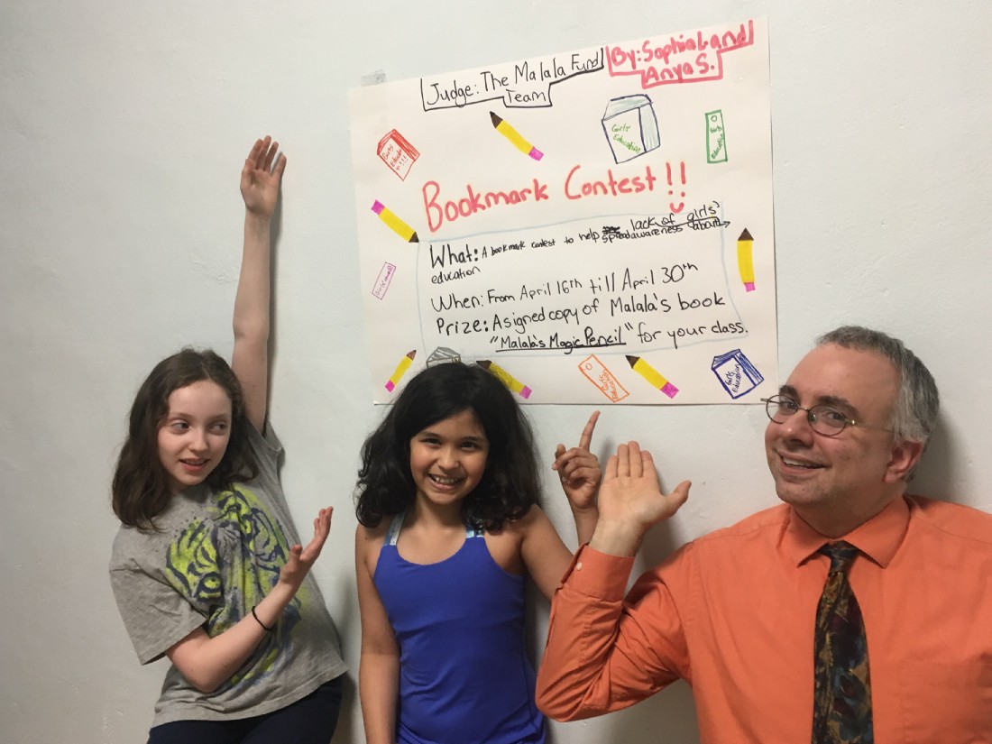 Anya (centre) poses with her friend Sophia (far left) and teacher Mr. Storti in front of a poster advertising the bookmark contest. (Courtesy of Anya Sen)