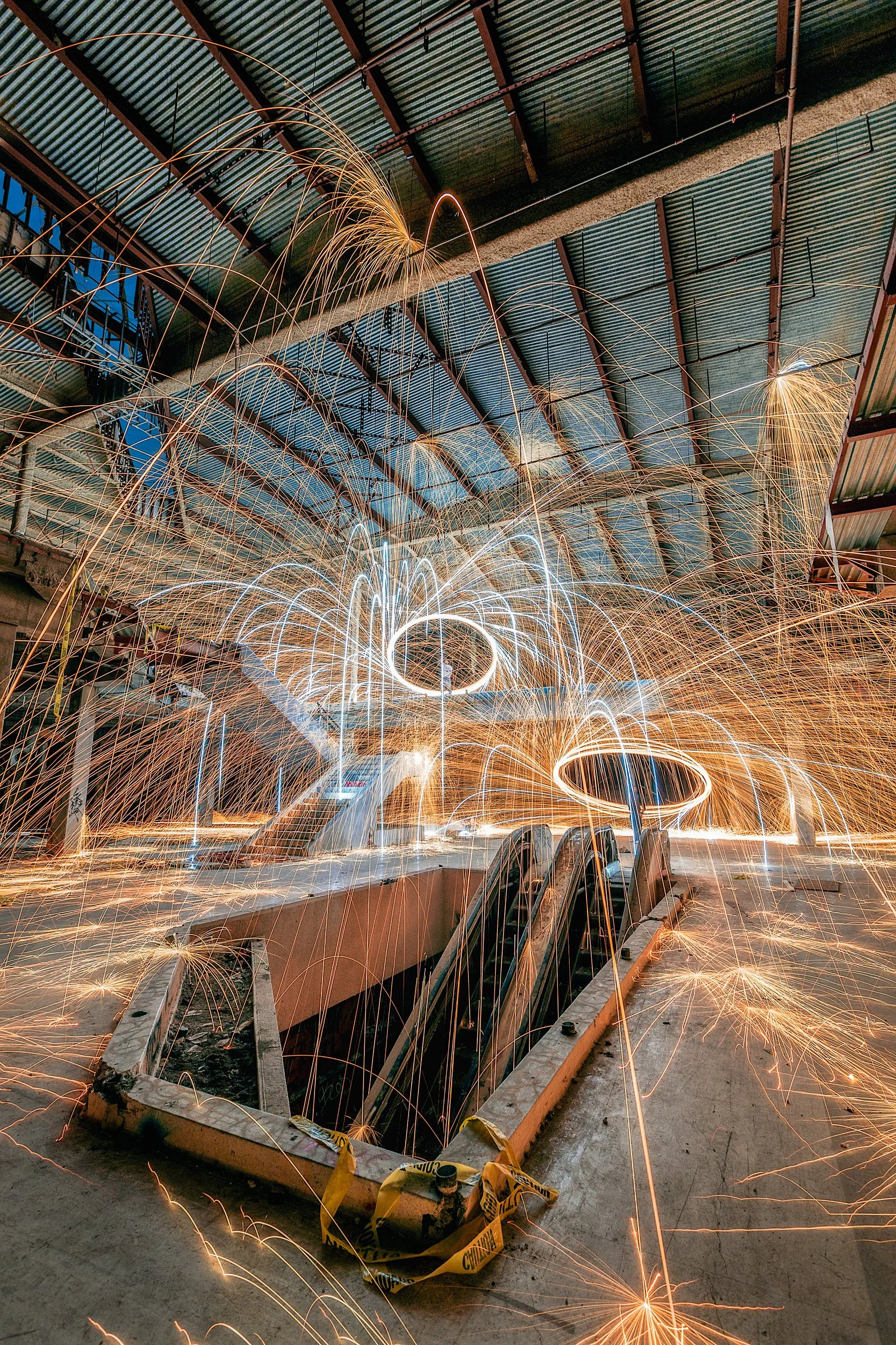 Long exposure photo of spinning steel wool sparks inside a gutted, abandoned Los Angeles shopping mall with escalators by Chris Ewen Crosby.