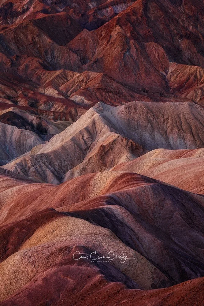 Vertical abstract landscape of Death Valley badlands at sunrise with pink light on brown and tan rippling sediment peaks.