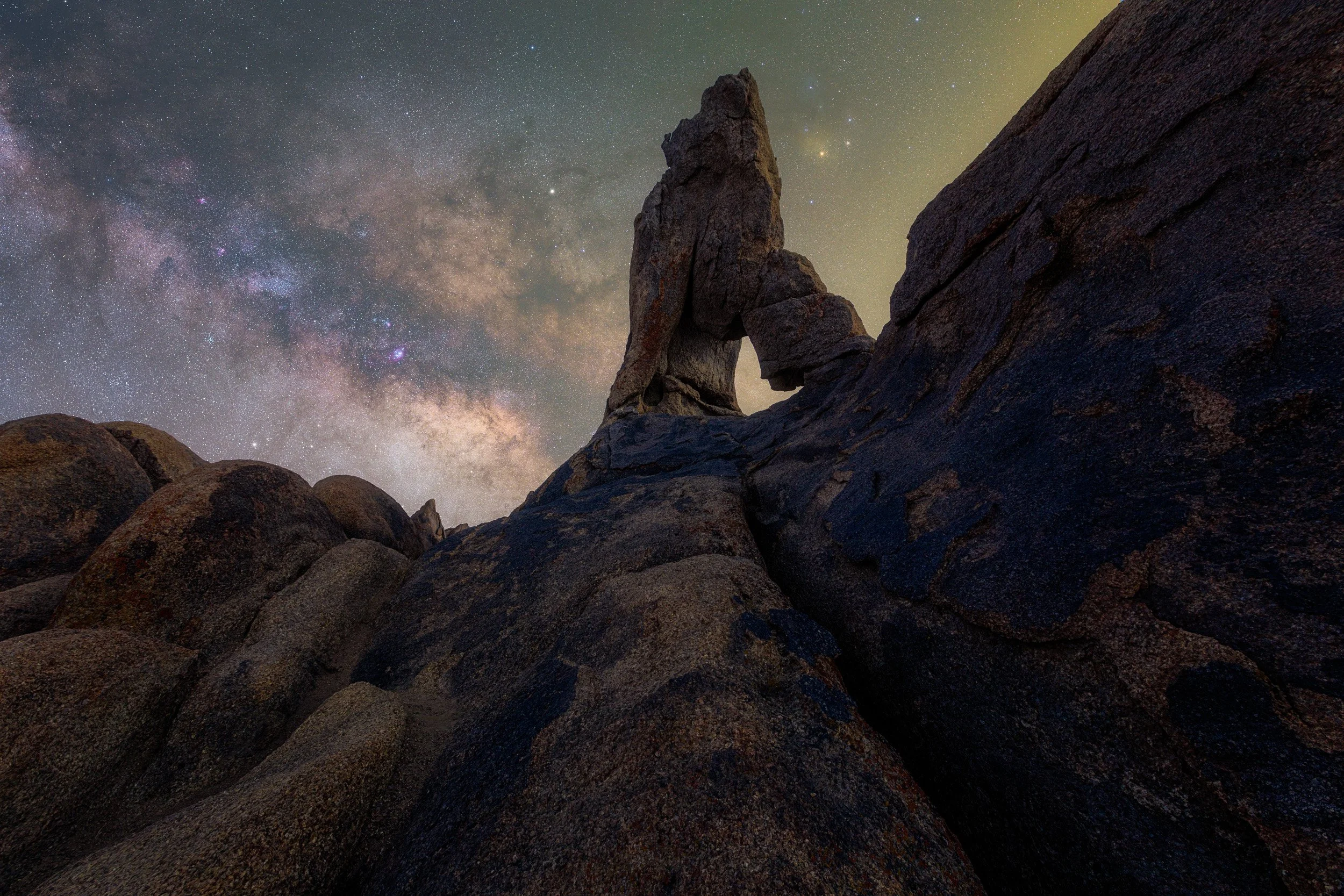 Horizontal night astrophotography photograph of a dramatic granite rock arch silhouetted against the bright core of the Milky Way galaxy in the Alabama Hills near Lone Pine, California by Chris Ewen Crosby.