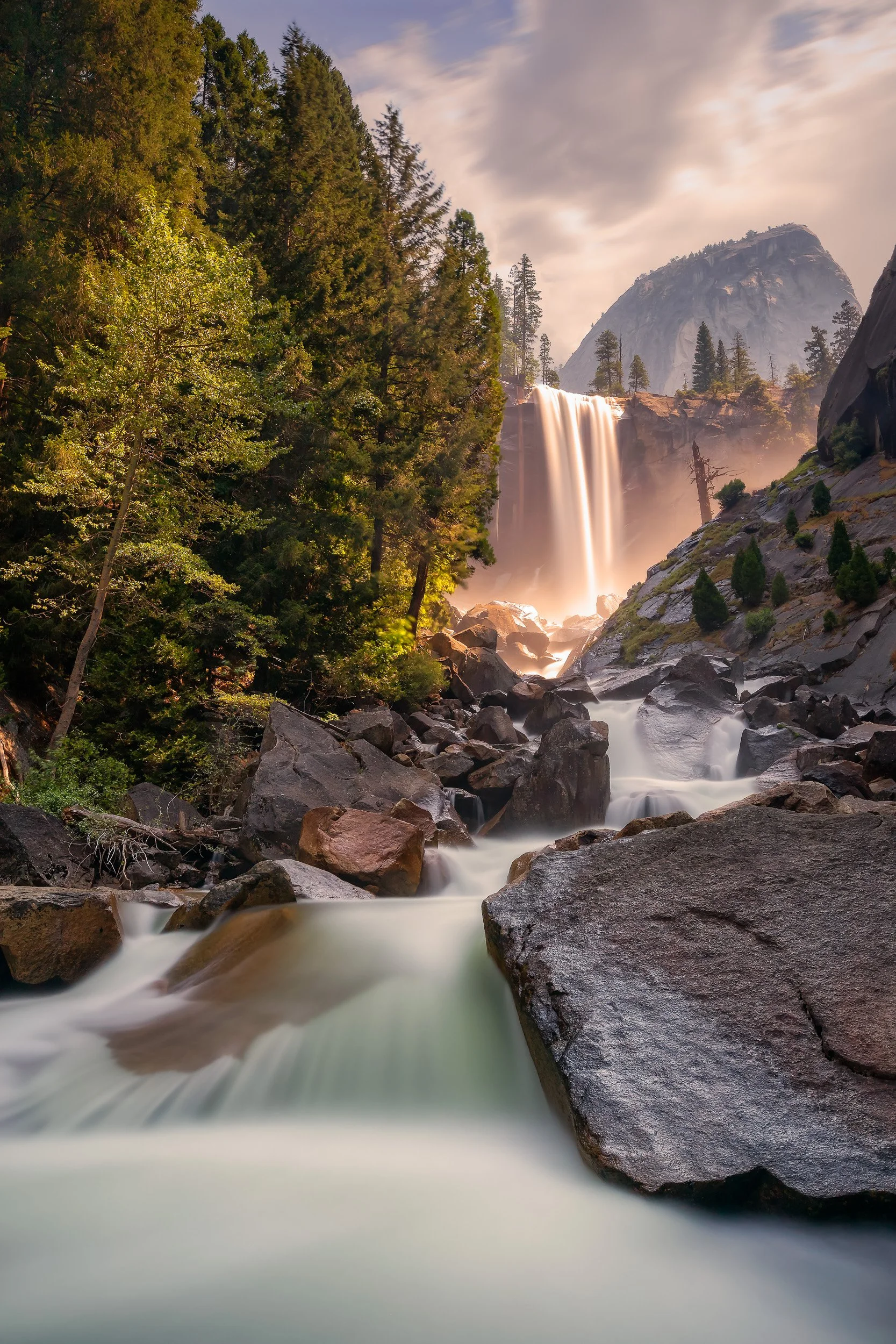 Vertical long-exposure landscape photograph of Vernal Fall cascading into the Merced River below Liberty Cap under a warm sky in Yosemite National Park by Chris Ewen Crosby.