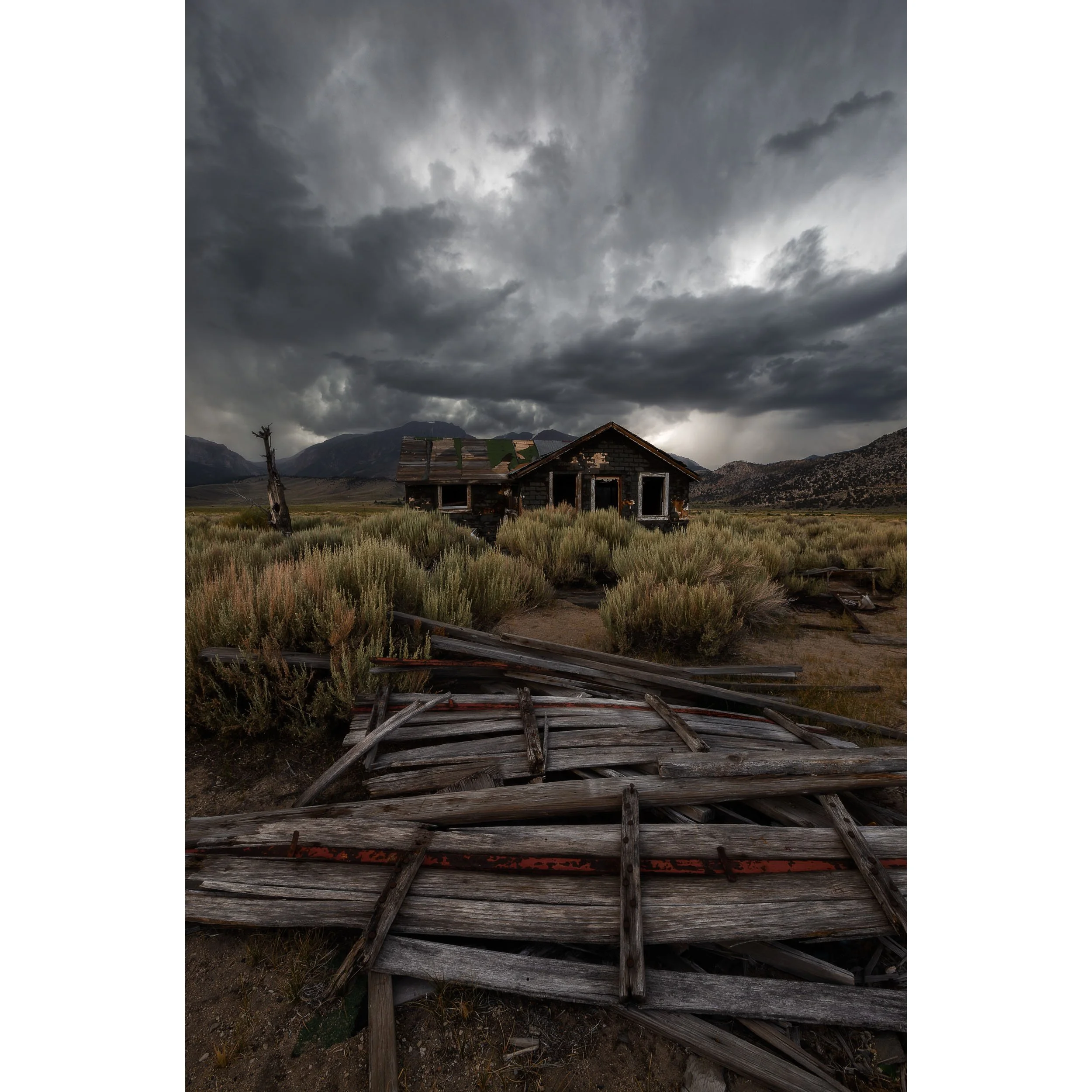 Vertical fine art landscape photograph of an abandoned wooden cabin under dramatic dark storm clouds in the Eastern Sierra.
