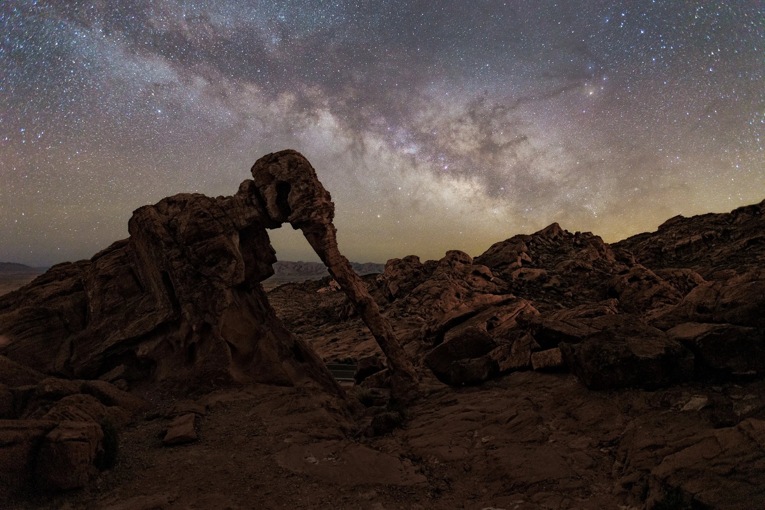 Horizontal night astrophotography photograph of the famous Elephant Rock formation silhouetted beneath the Milky Way galaxy in Valley of Fire State Park, Nevada by Chris Ewen Crosby.